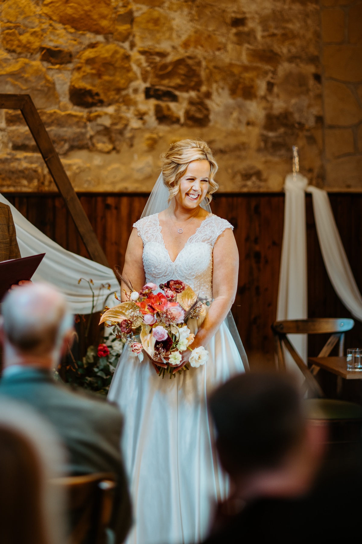 smiling bride with blonde hair wearing white lace dress and holding floral bouquet during ceremony scottish humanist wedding