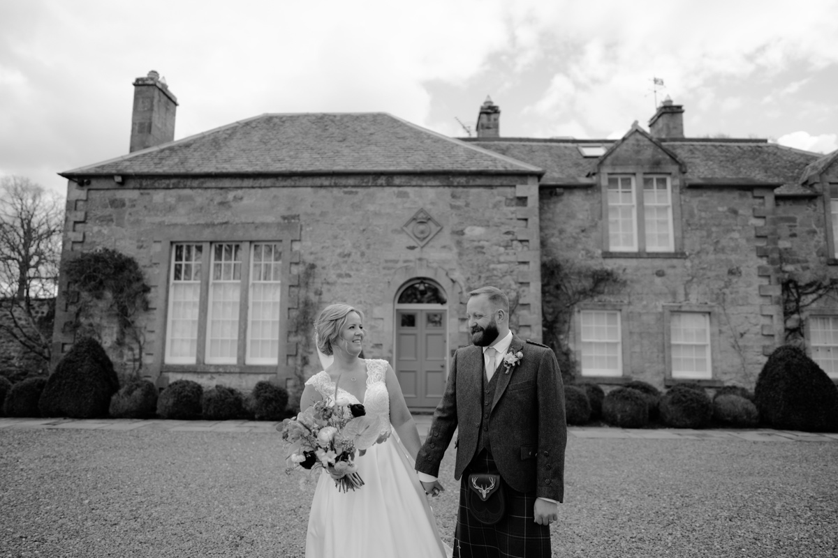 black and white photo of bride and groom holding hands in front of rosebery steadings scottish humanist wedding