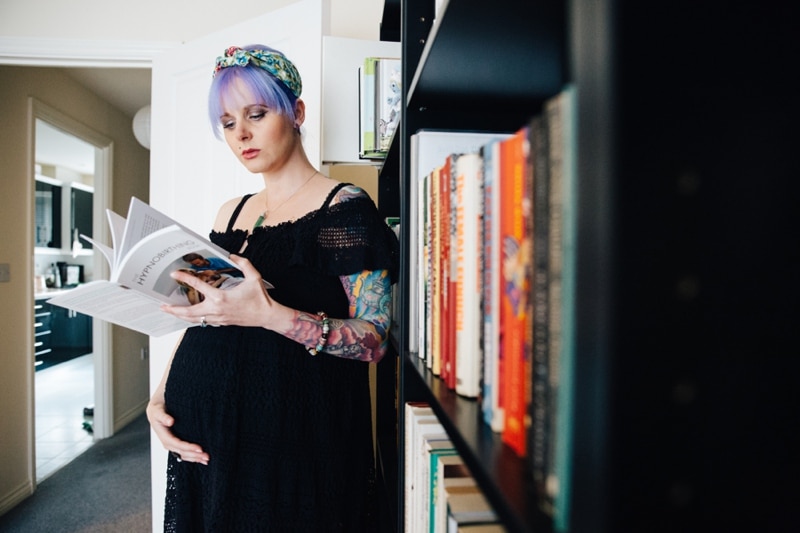 Alternative tattoo mum at her Coventry Maternity Photoshoot standing by bookshelf reading about Hypnobirthing