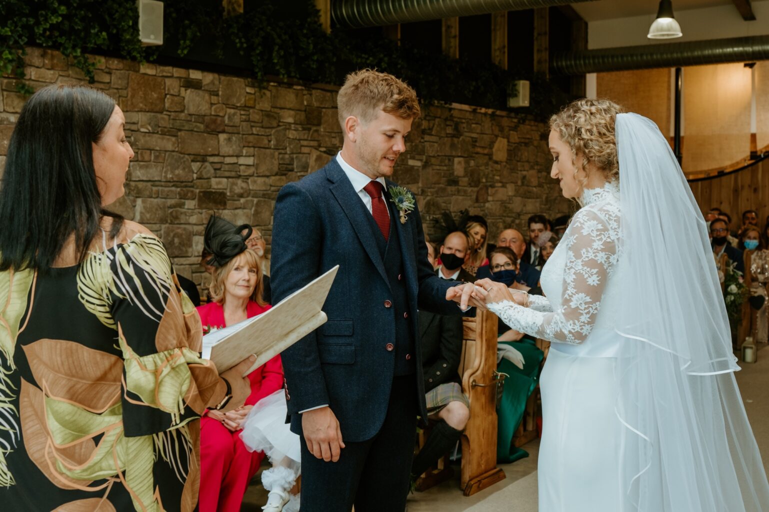 bride wearing white dress placing wedding ring on grooms finger at ceremony in barn wedding venue scotland cairns farm estate wedding