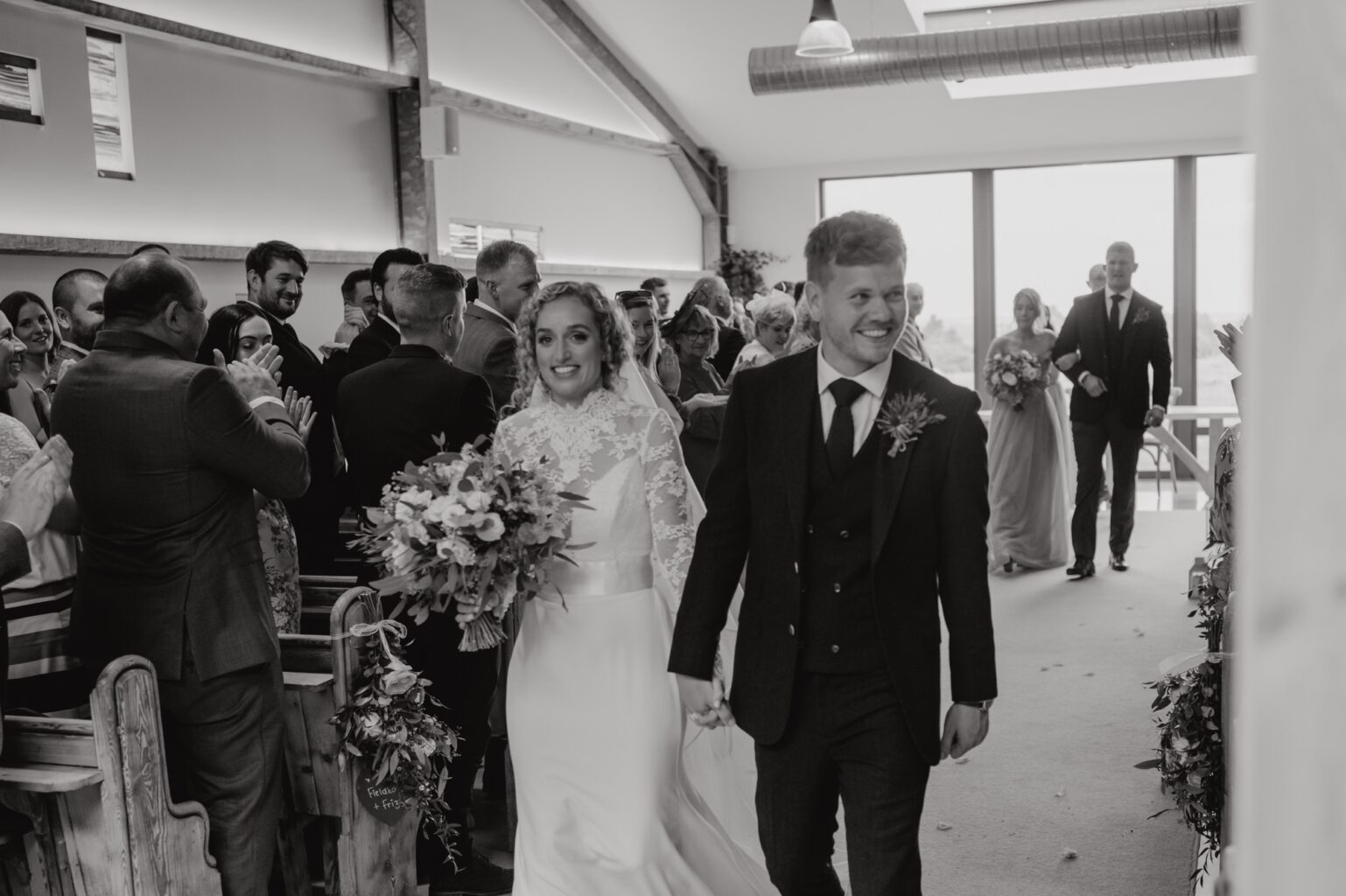 just married bride and groom walking back down the aisle holding hands and smiling black and white photo cairns farm estate wedding