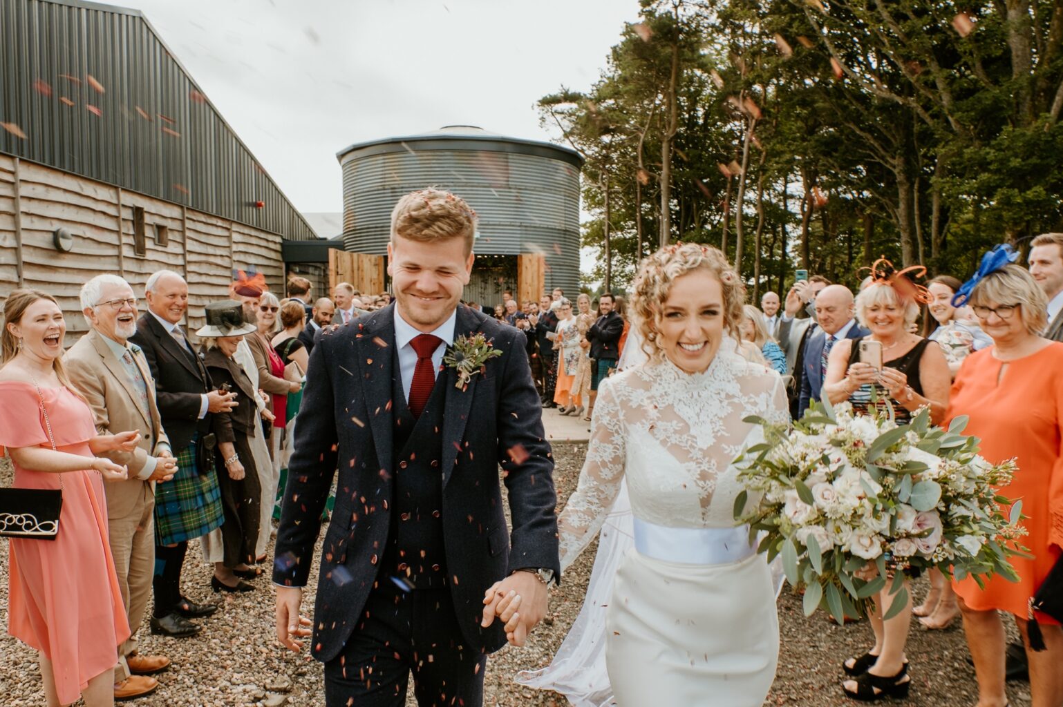 bride and groom walking towards camera as guests throw confetti at them as they walk out of barn wedding venue cairns farm estate wedding scotland