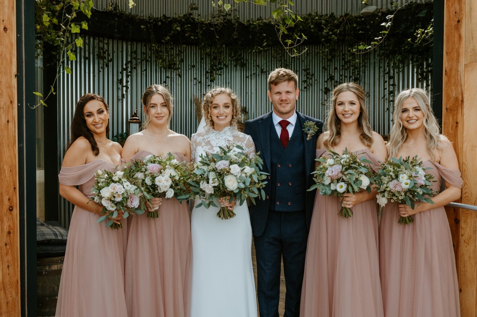 bride and groom in group picture with four bridesmaids bride and bridesmaids all holding bouquets cairns farm estate wedding