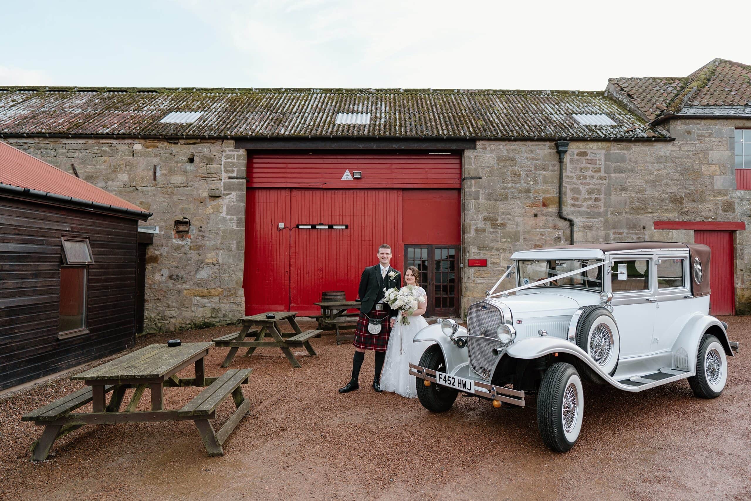 kinkell byre wedding photos exterior outside view of farm barn wedding venue st andrews scotland bride and groom with classic car