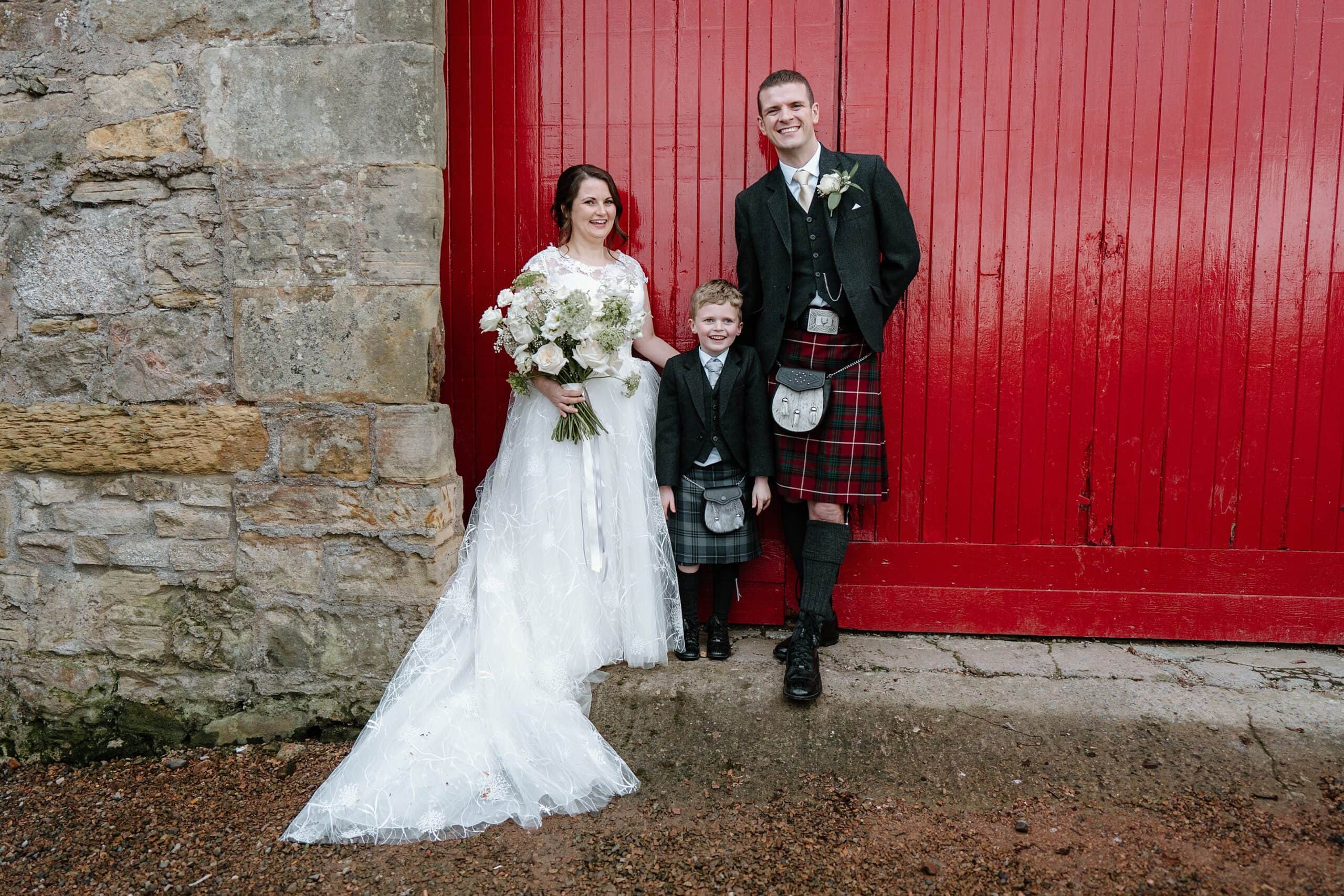 kinkell byre wedding photos of bride and groom outside venue with red barn doors in background at st andrews wedding venue