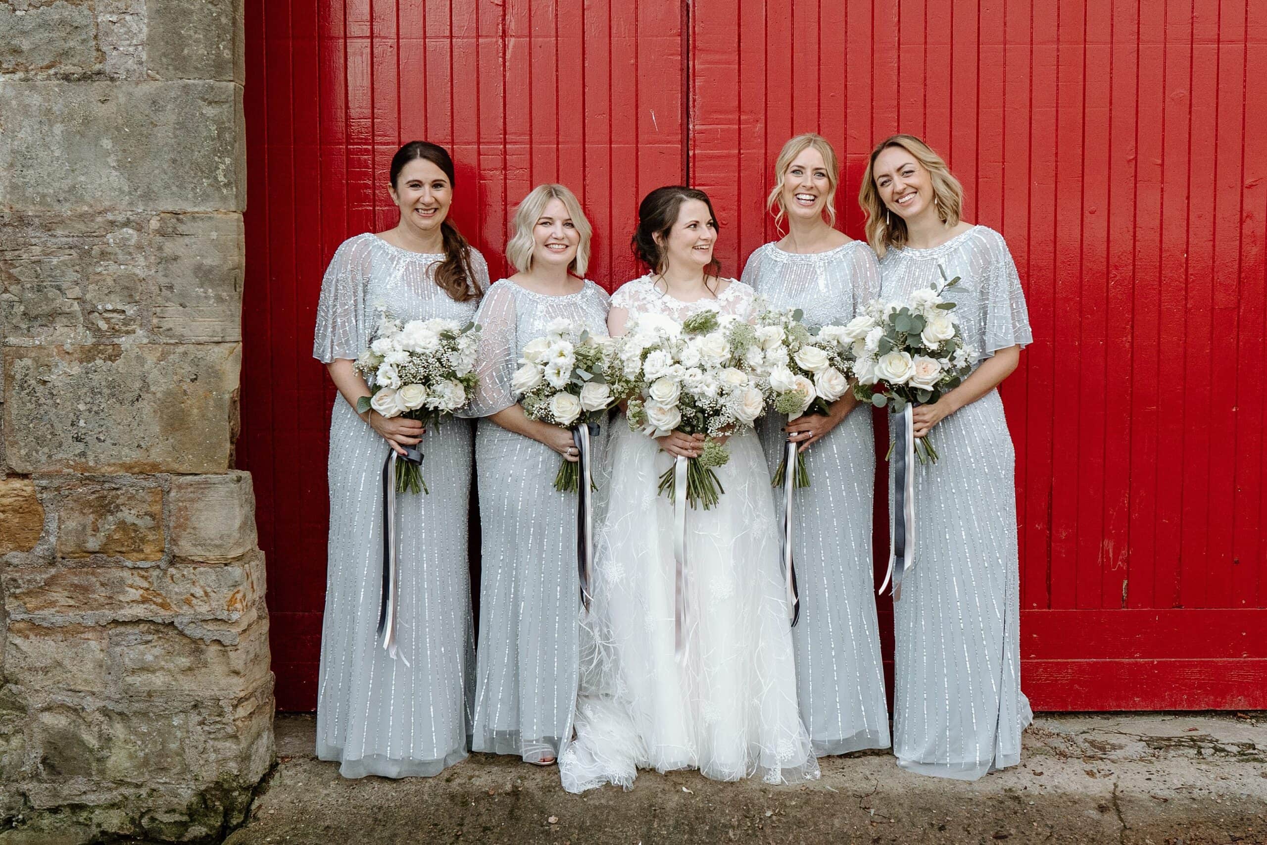 kinkell byre wedding photos of bride and bridesmaids outside venue with red barn doors in background at st andrews wedding venue