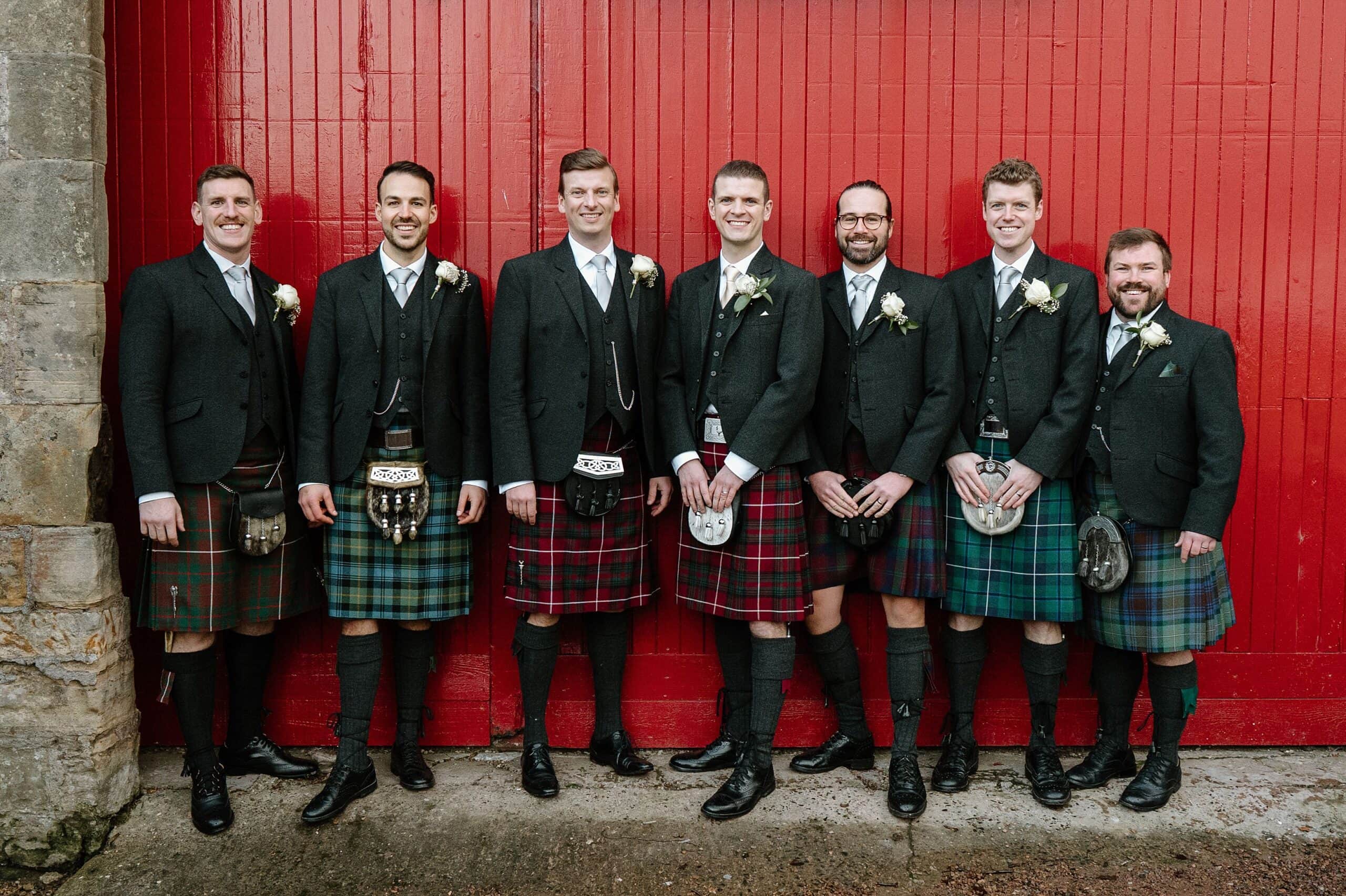 kinkell byre wedding photos of groom and groomsmen outside venue with red barn doors in background at st andrews wedding venue