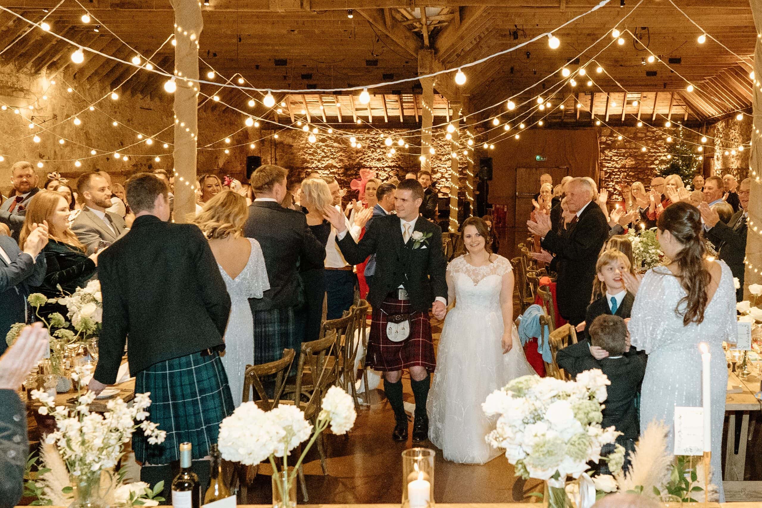 kinkell byre wedding photos interior inside view of farm barn wedding venue st andrews scotland reception dinner setup with fairy lights and long trestle tables and bride and groom entrance to dinner reception