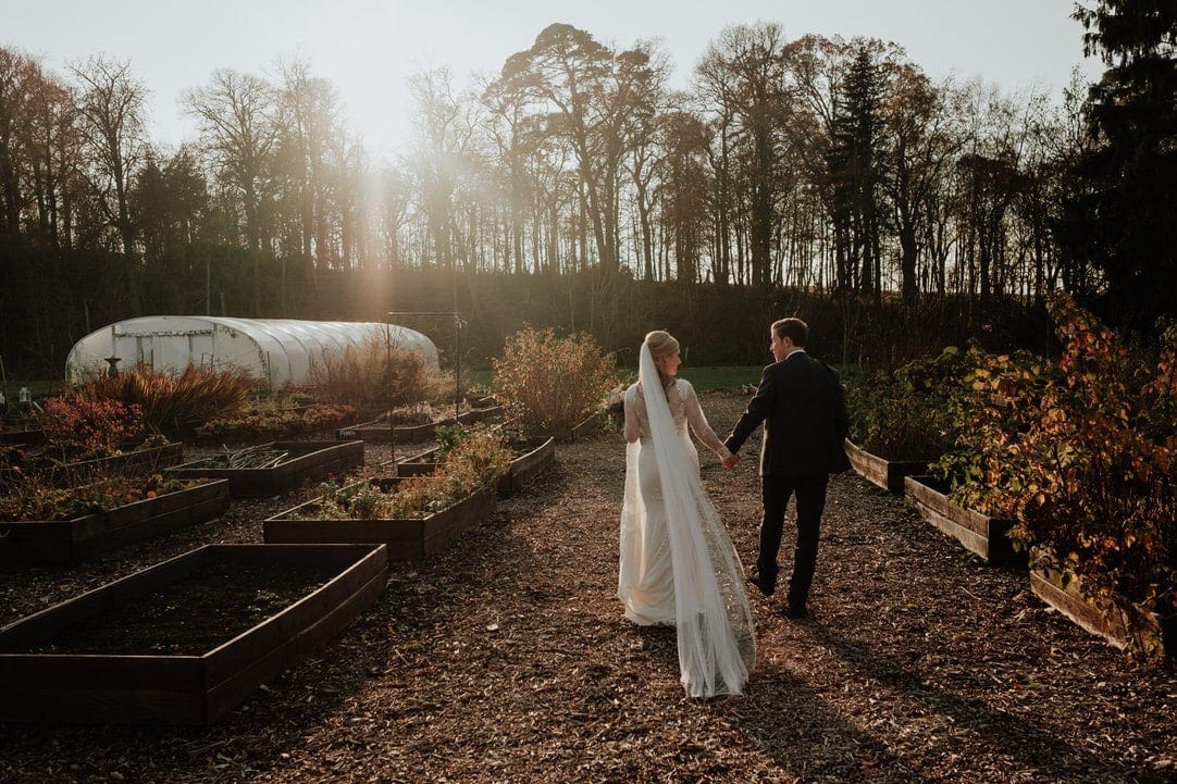 bride and groom walk through walled garden at colstoun house captured by wedding photographer east lothian based