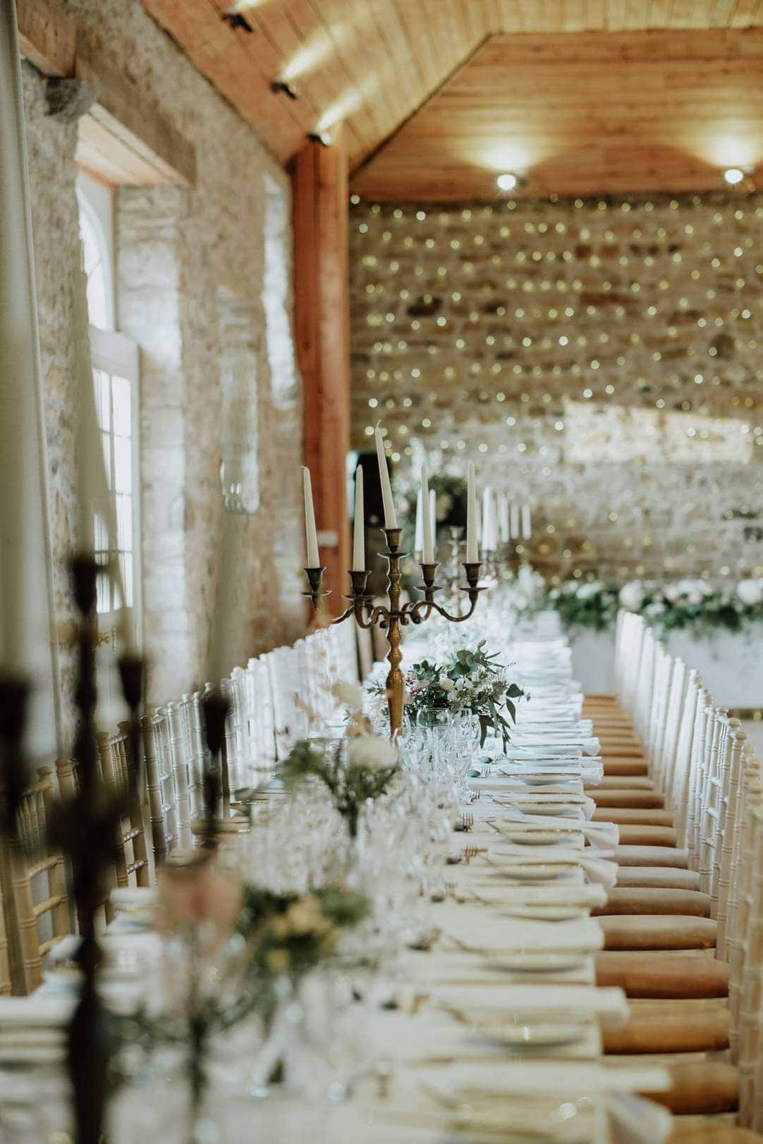 colstoun house wedding set up for a sinner reception indoors with long tables with candles on it against a stane brick wall