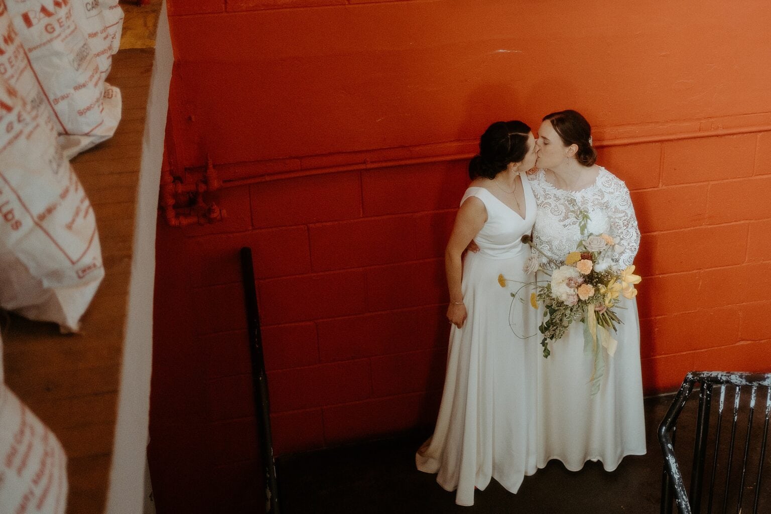 brides kissing in front of orange wall inside venue west on the green wedding scotland