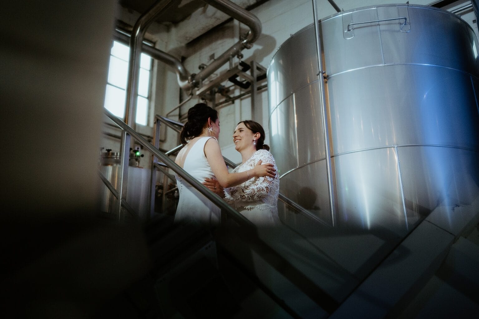 brides looking into each others eyes as they stand infront of metal tank in brewing room west on the green wedding