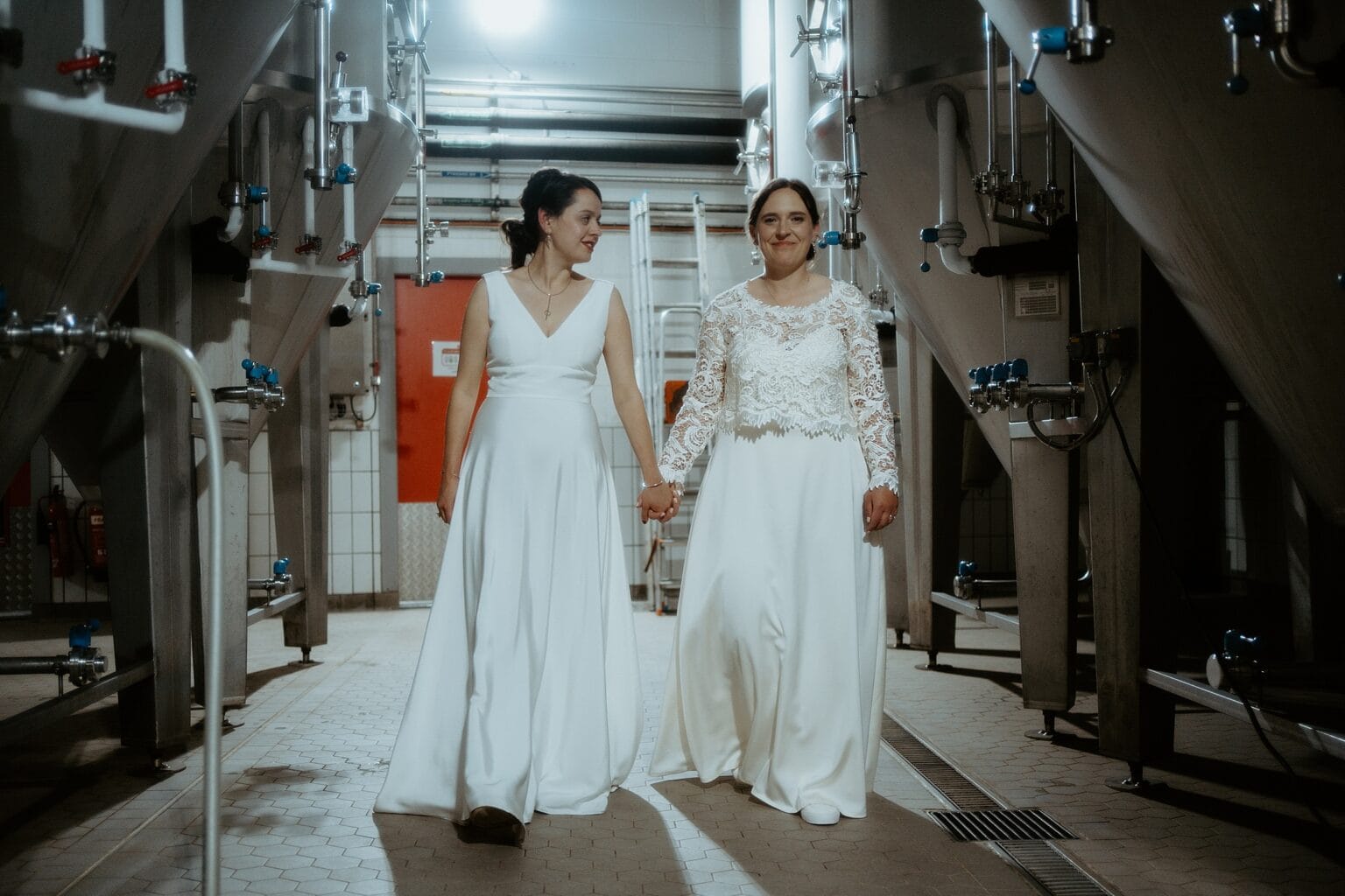 brides wearing long white dresses holding hands walking towards camera through brewing room west on the green wedding glasgow