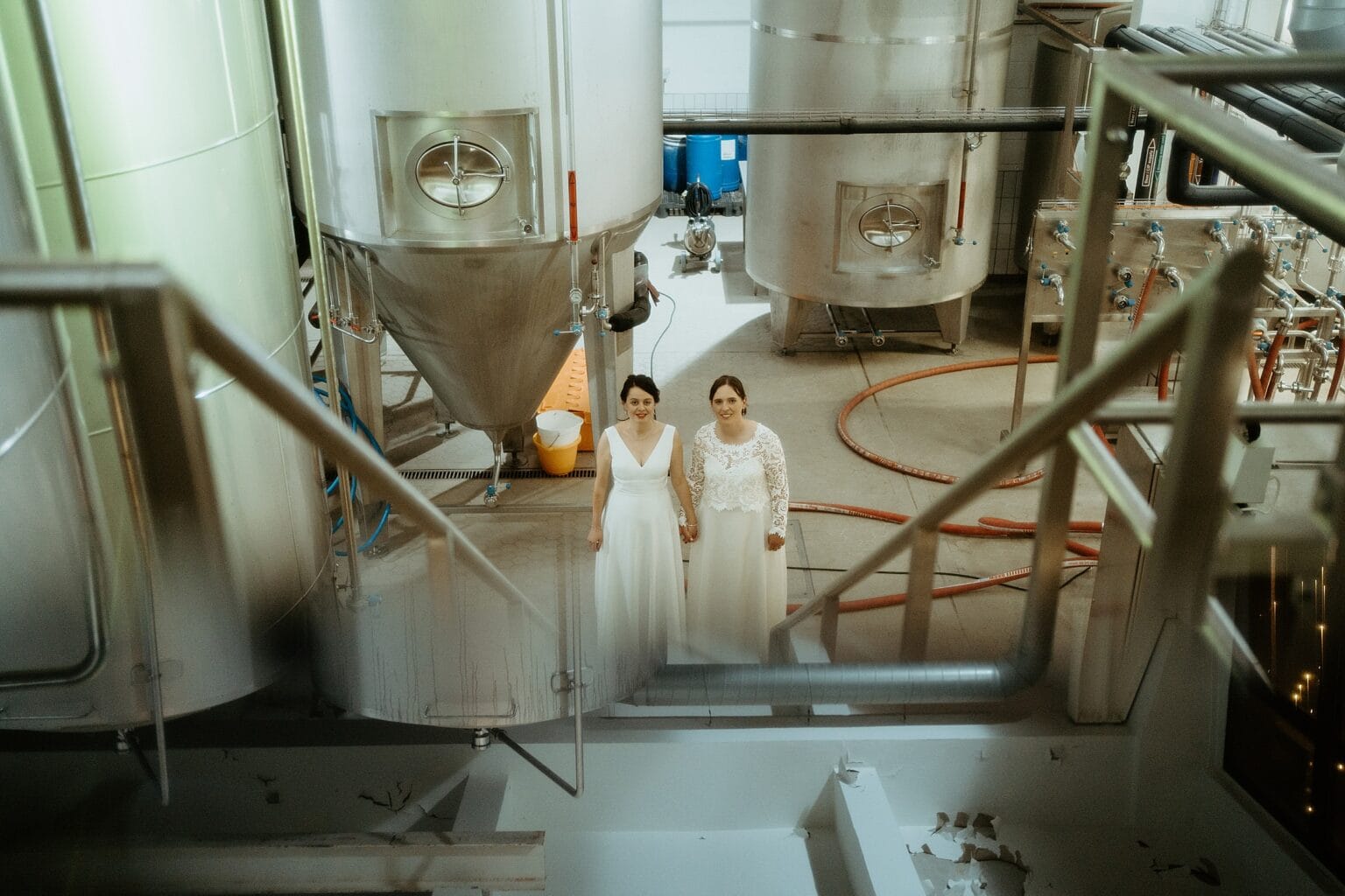 brides looking at camera as they stand infront of metal tanks in brewing room west on the green wedding unique wedding venues glasgow