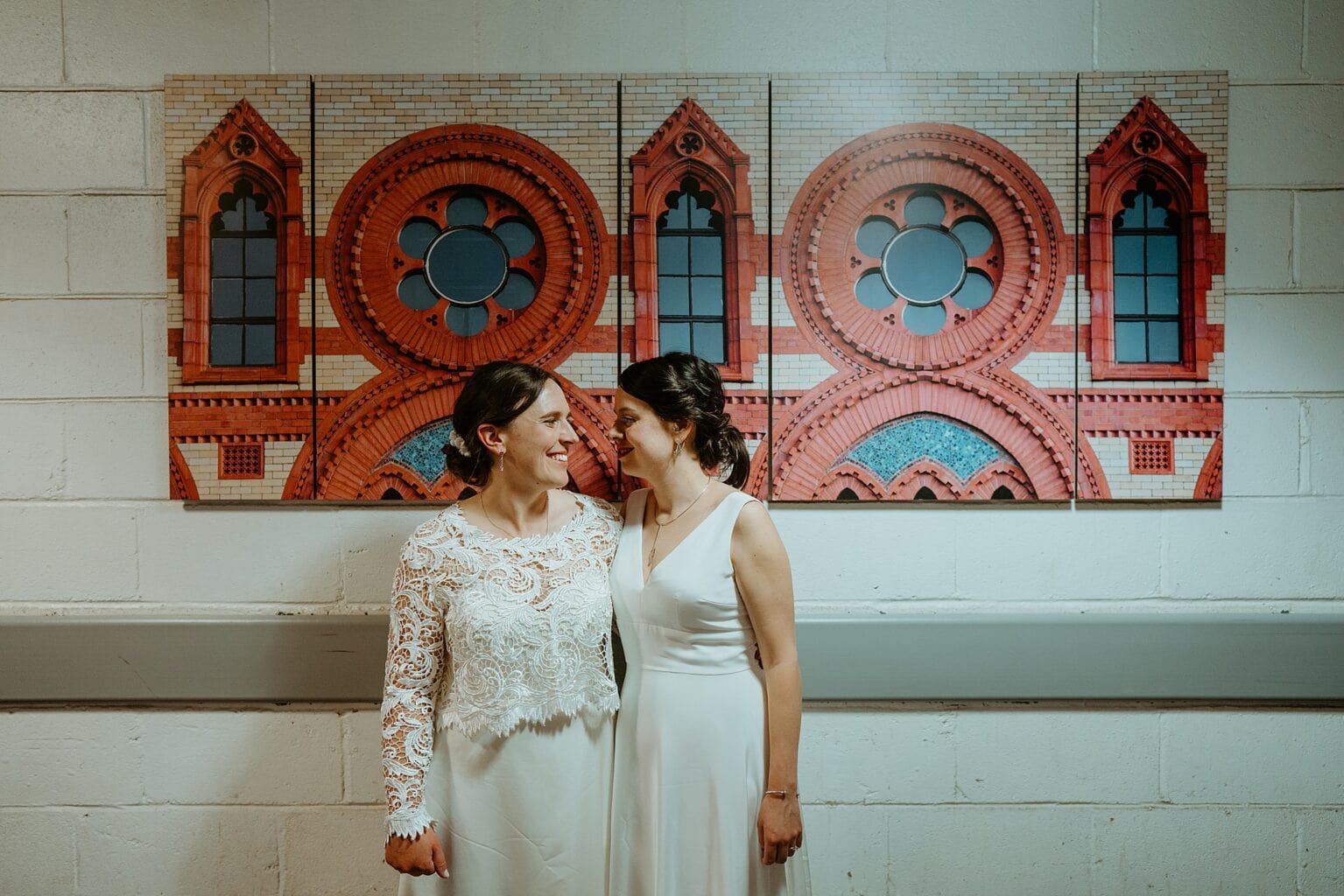 brides wearing white dresses standing in hall in front of red and blue artwork west on the green wedding scotland