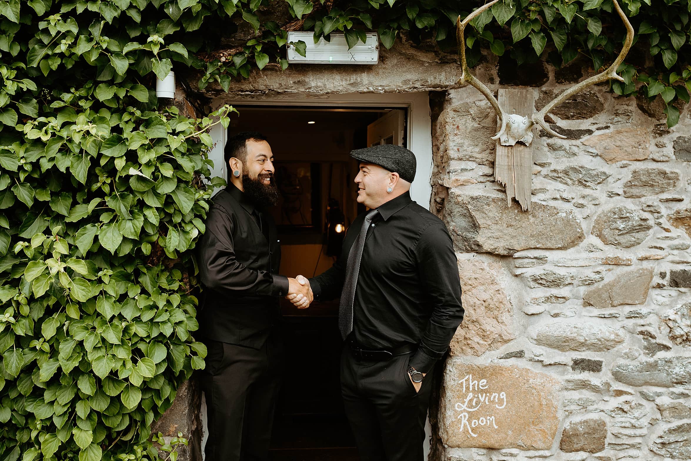 groom and best man dressed in black standing in door way with ivy growing up wall monachyle mhor wedding