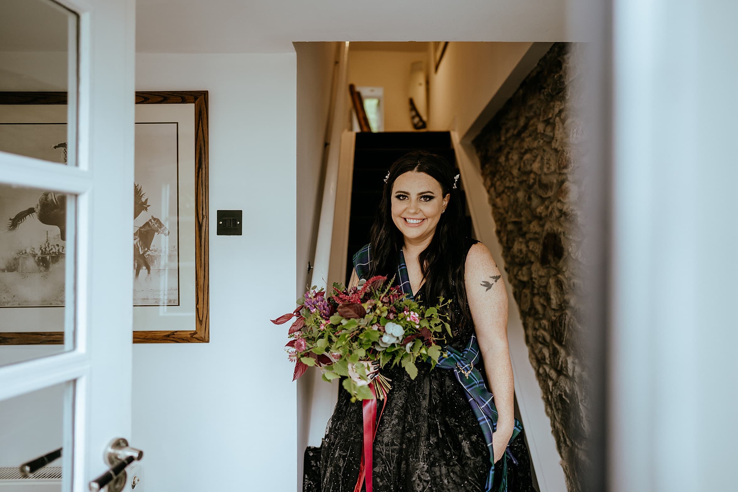 bride to be at bottom of stairs holding bouquet and smiling at camera monachyle mhor wedding