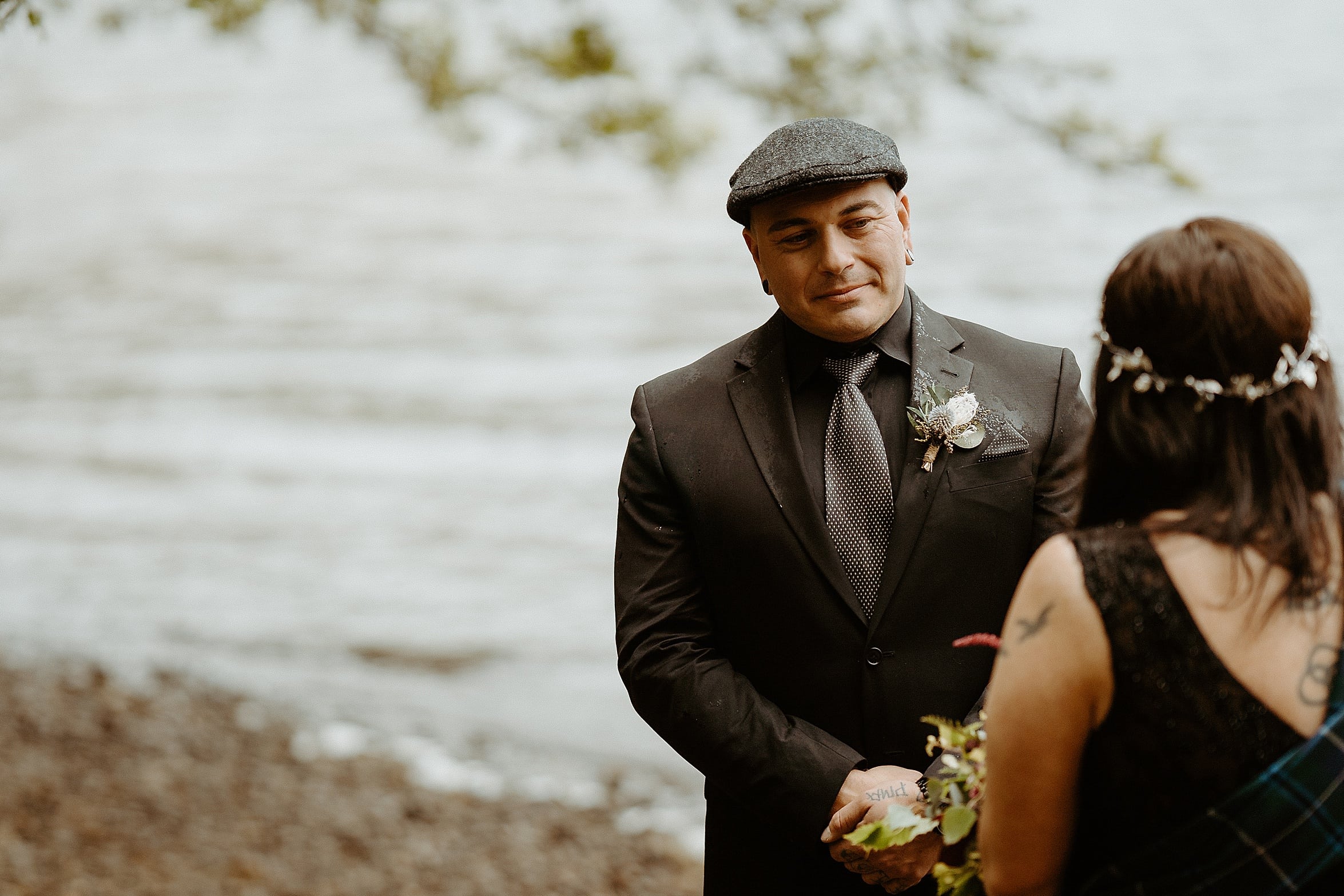 close up of groom wearing black suit and flat cap with loch in background monachyle mhor wedding