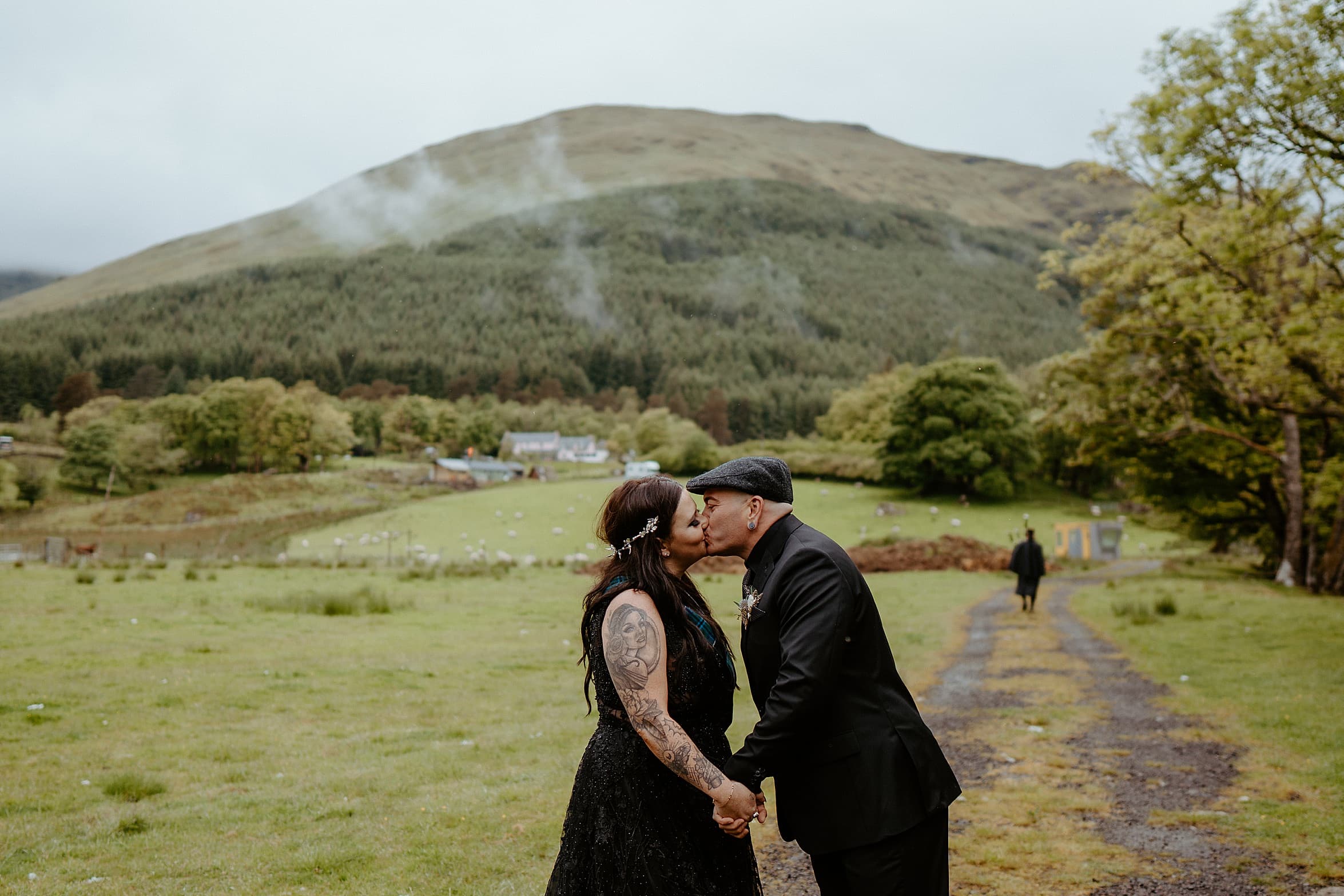 bride and groom holding hands and kissing with green fields and mountains in background monachyle mhor wedding