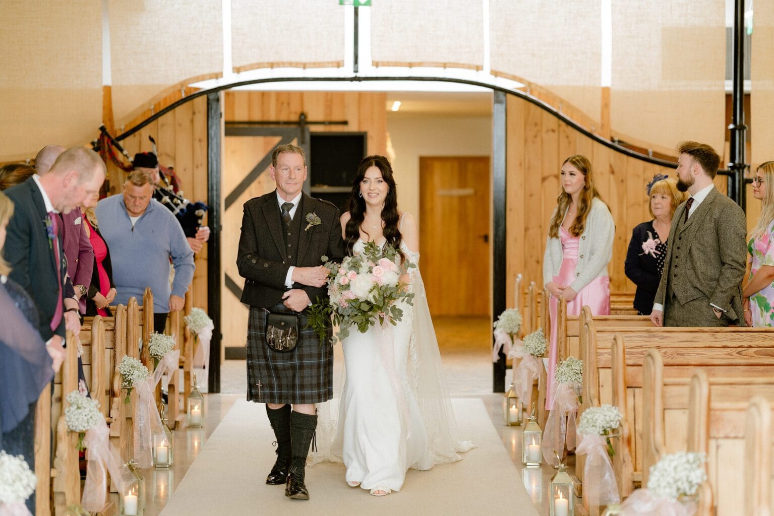 guests stand and watch as the bride and her father walk down the aisle arm in arm at barn wedding venues west lothian scotland