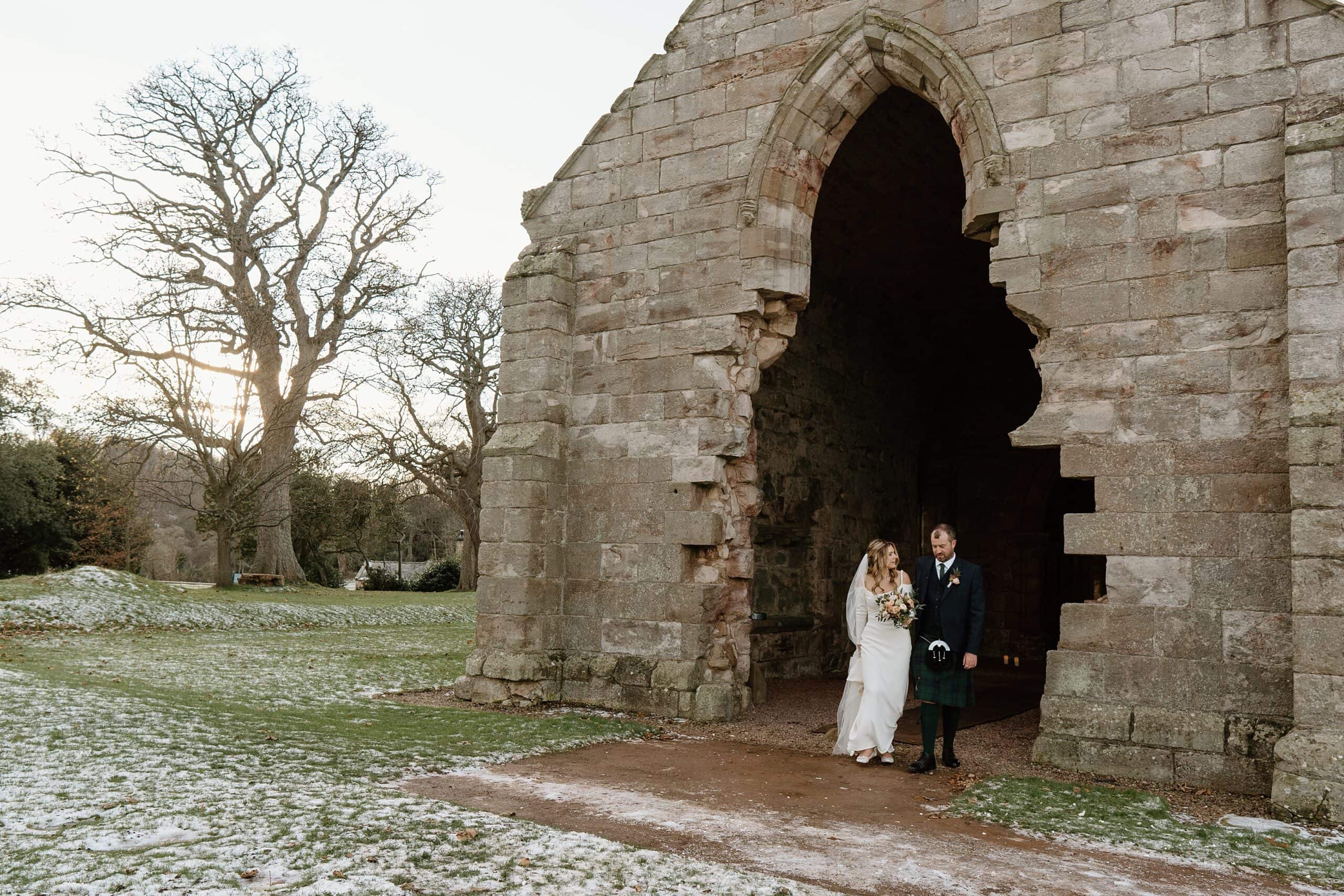 external outside view of dunglass estate wedding photos chapel church scotland on snowy winter day with bride and groom smiling at doorway