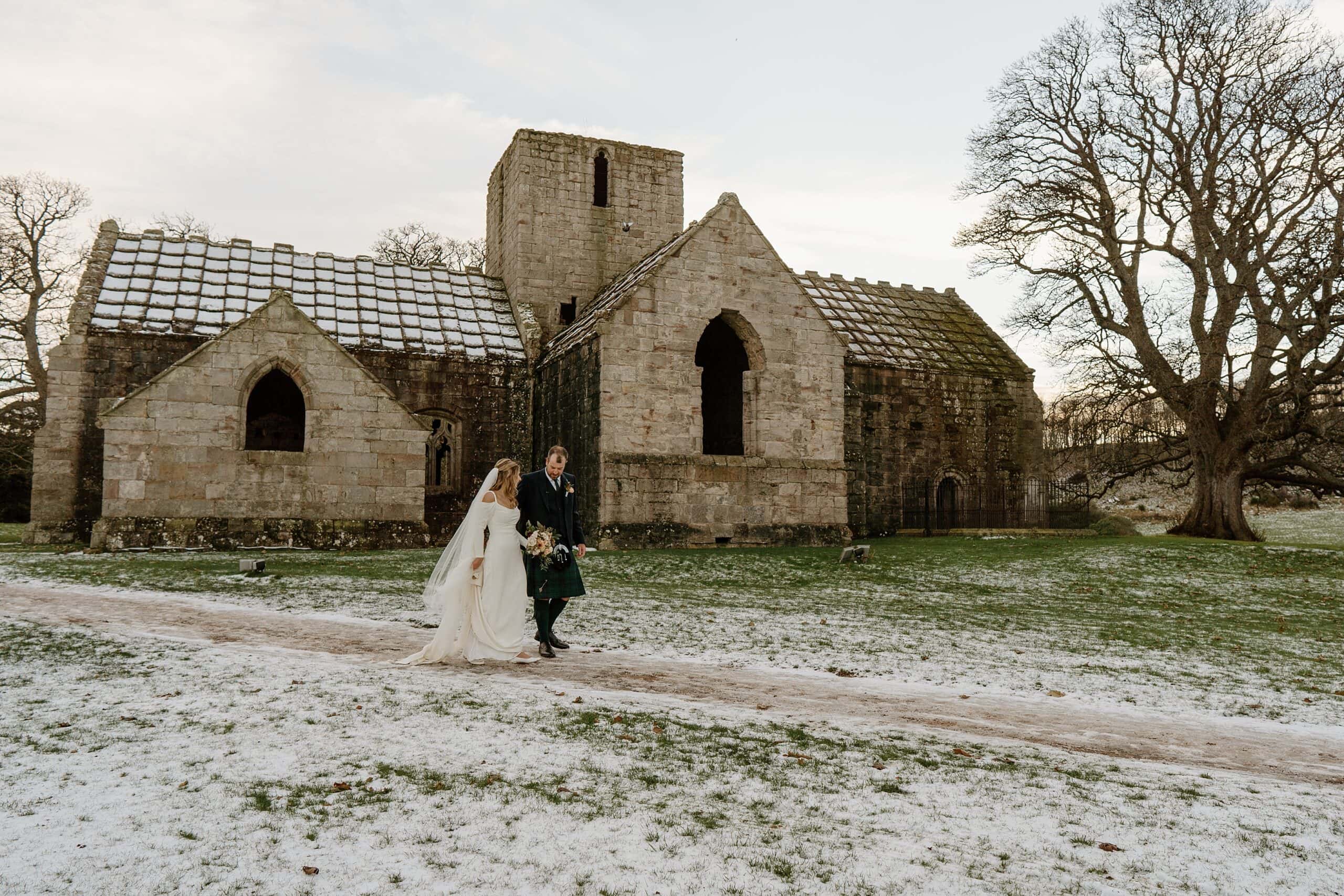 external outside view of dunglass estate wedding photos chapel church scotland on snowy winter day with bride and groom smiling and walking
