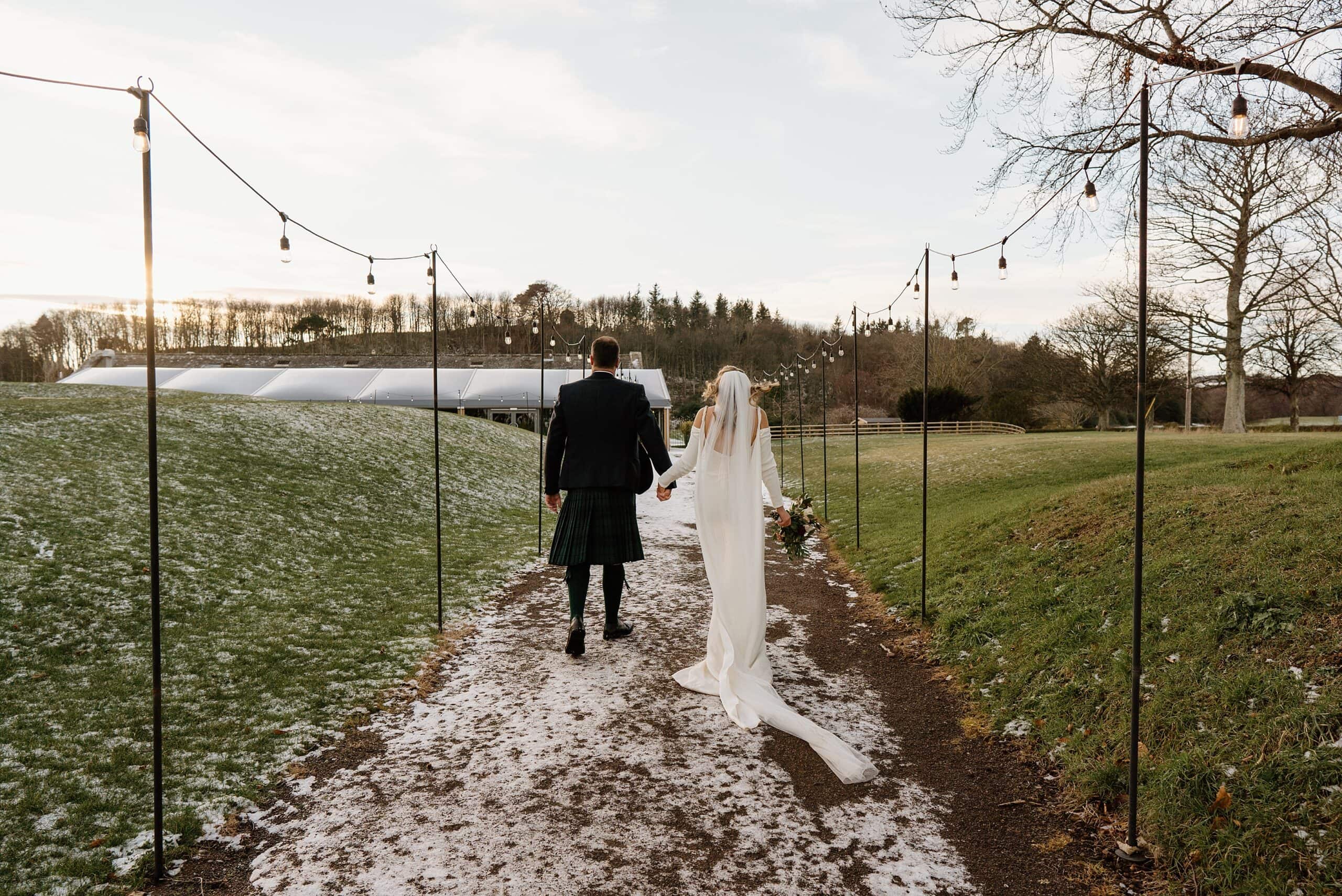 external outside view of dunglass estate wedding photos scotland on snowy winter day with bride and groom smiling and walking towards reception venue
