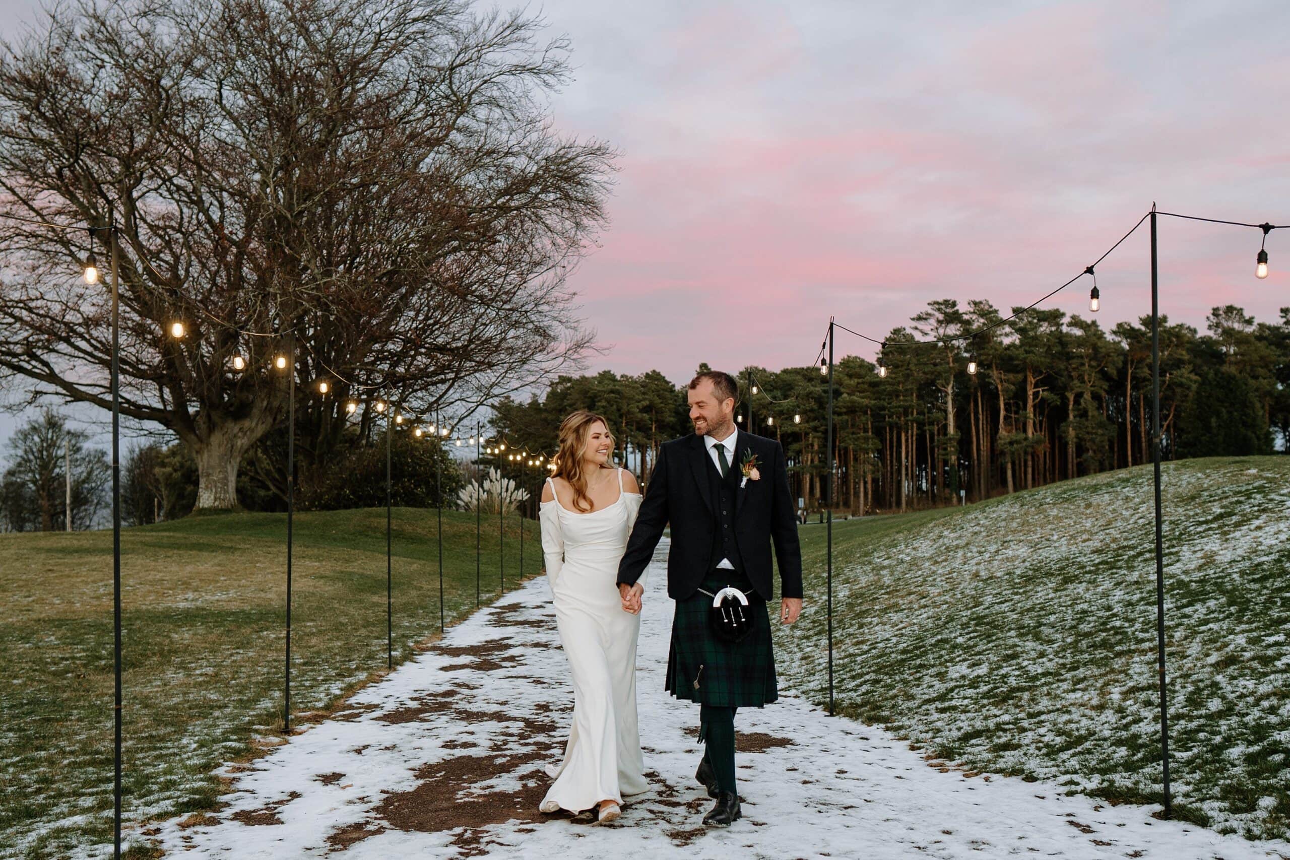 external outside view of dunglass estate wedding photos of bride and groom with festoon lighting on snowy winter day scotland