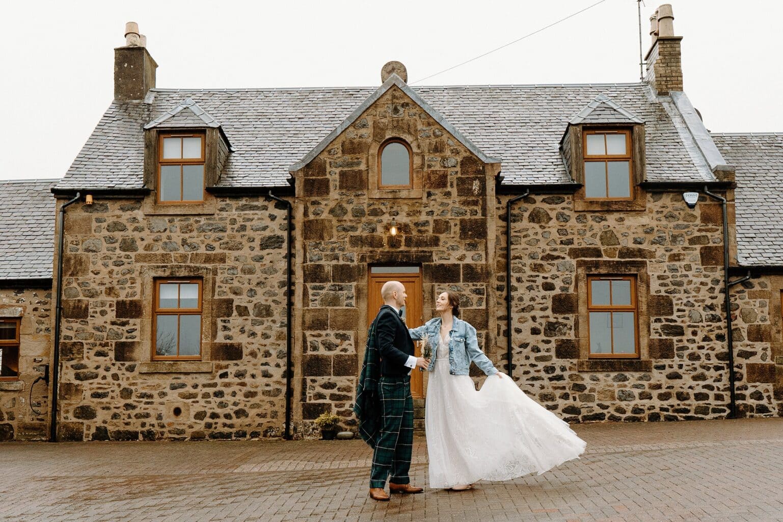 the bride and groom standing outside one of the top farm wedding venues scotland the bride is wearing a blue denim jacket