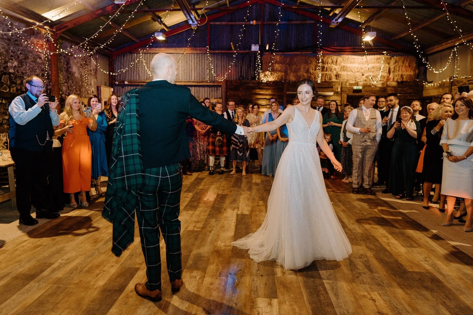 at their farm wedding venues scotland the bride and groom take the floor for their first dance as guests look on beneath festoon lighting
