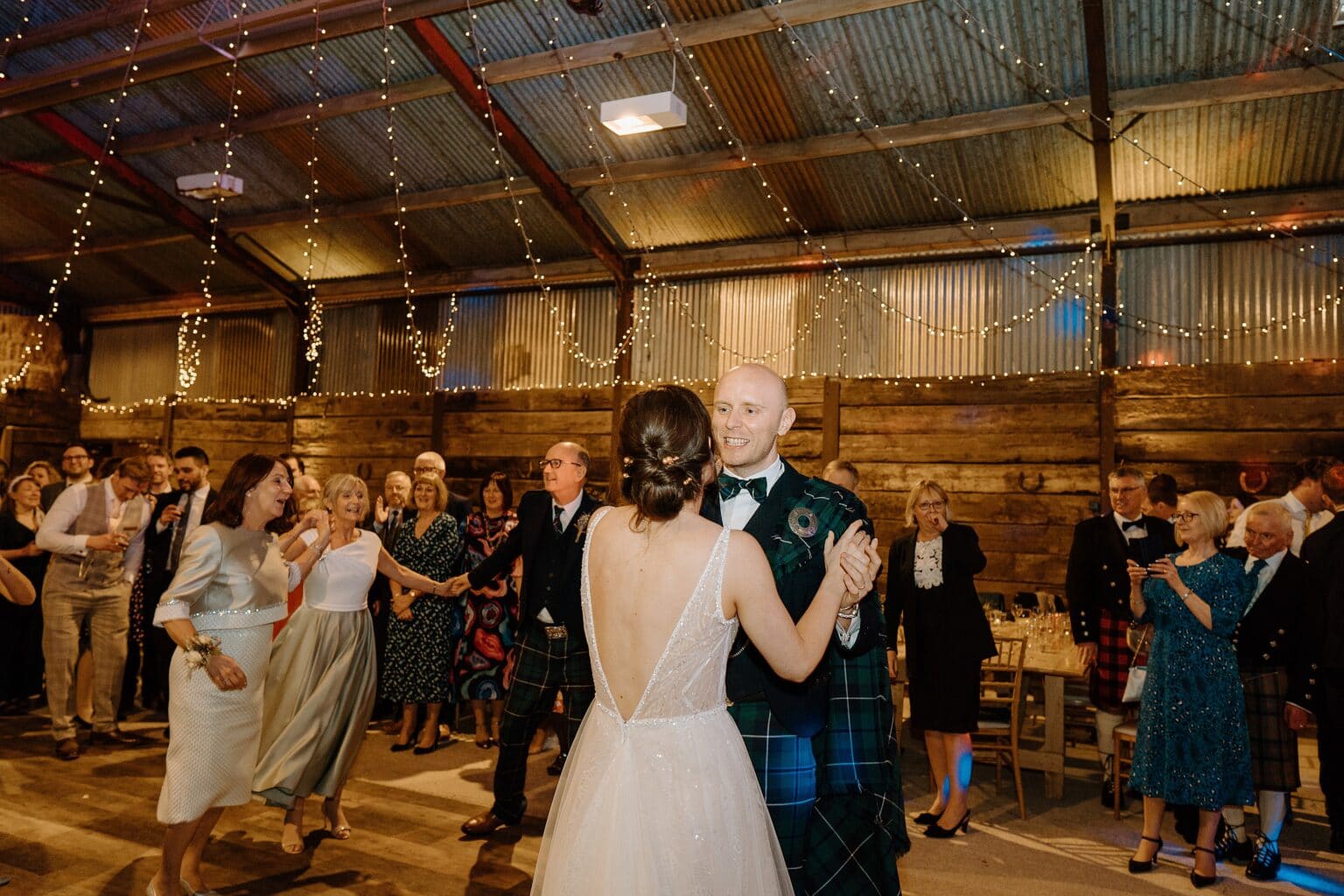 the bride and groom and guests dancing beneath festoon lighting at a wedding reception at a farm wedding venue near glasgow scotland