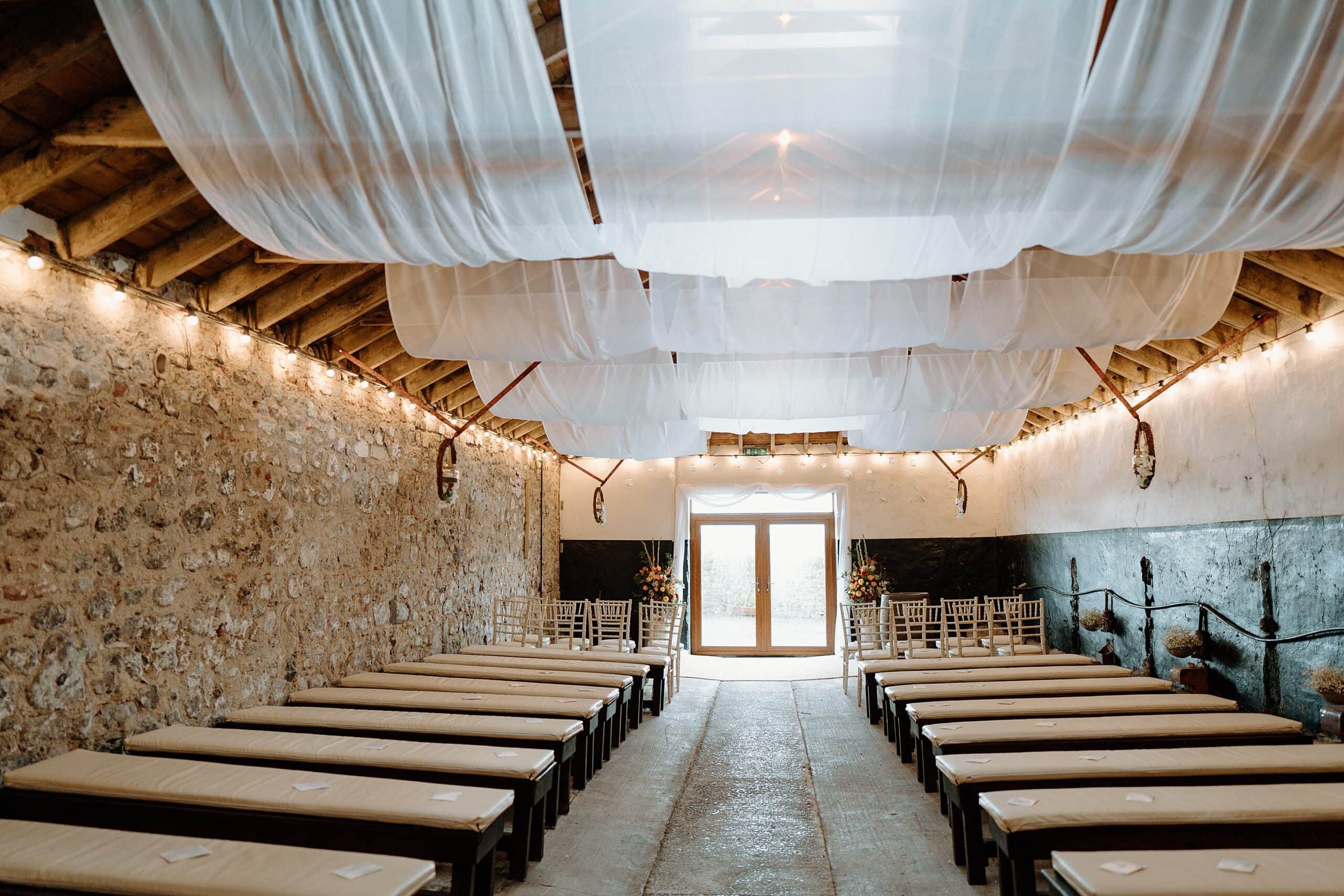 the wedding byre at harelaw farm wedding barn venue fenwick scotland set up for ceremony with seating and white drapes hanging from the ceiling