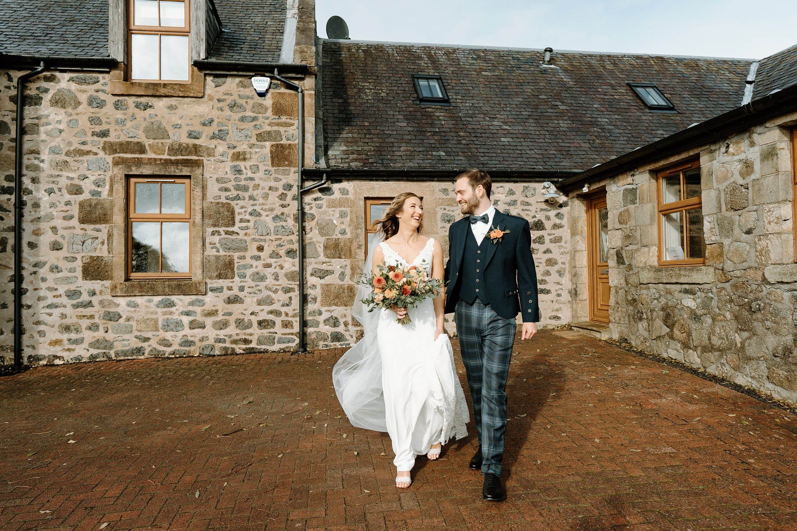 outside exterior view of harelaw farm wedding barn venue fenwick scotland showing bride and groom holding ands and smiling