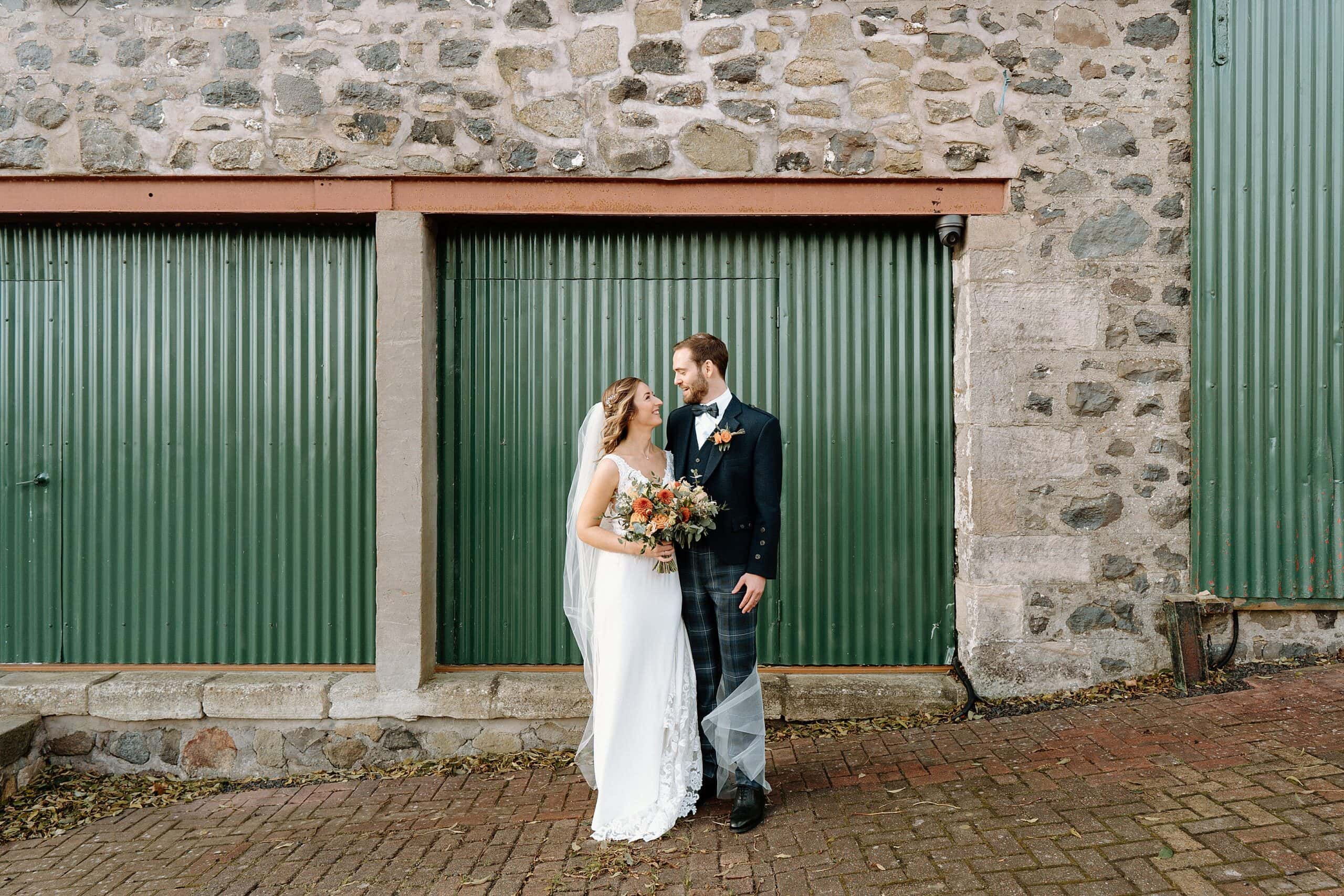 outside exterior view of harelaw farm wedding barn venue fenwick scotland showing bride and groom smiling in front of green barn doors