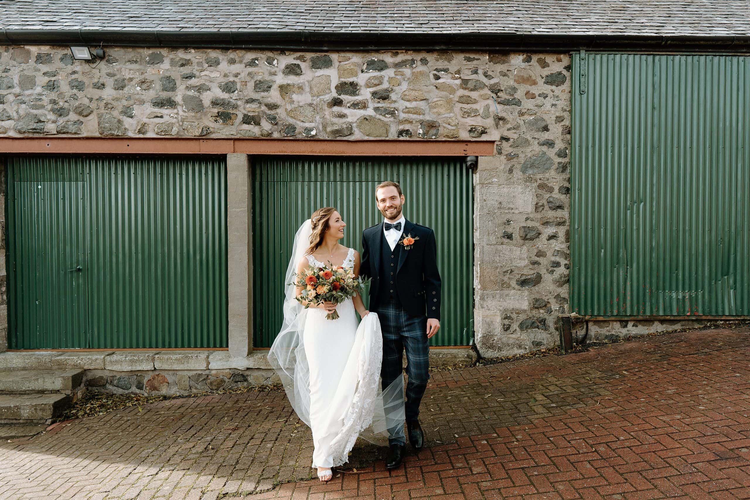 outside exterior view of harelaw farm wedding barn venue fenwick scotland showing bride and groom smiling in front of green barn doors