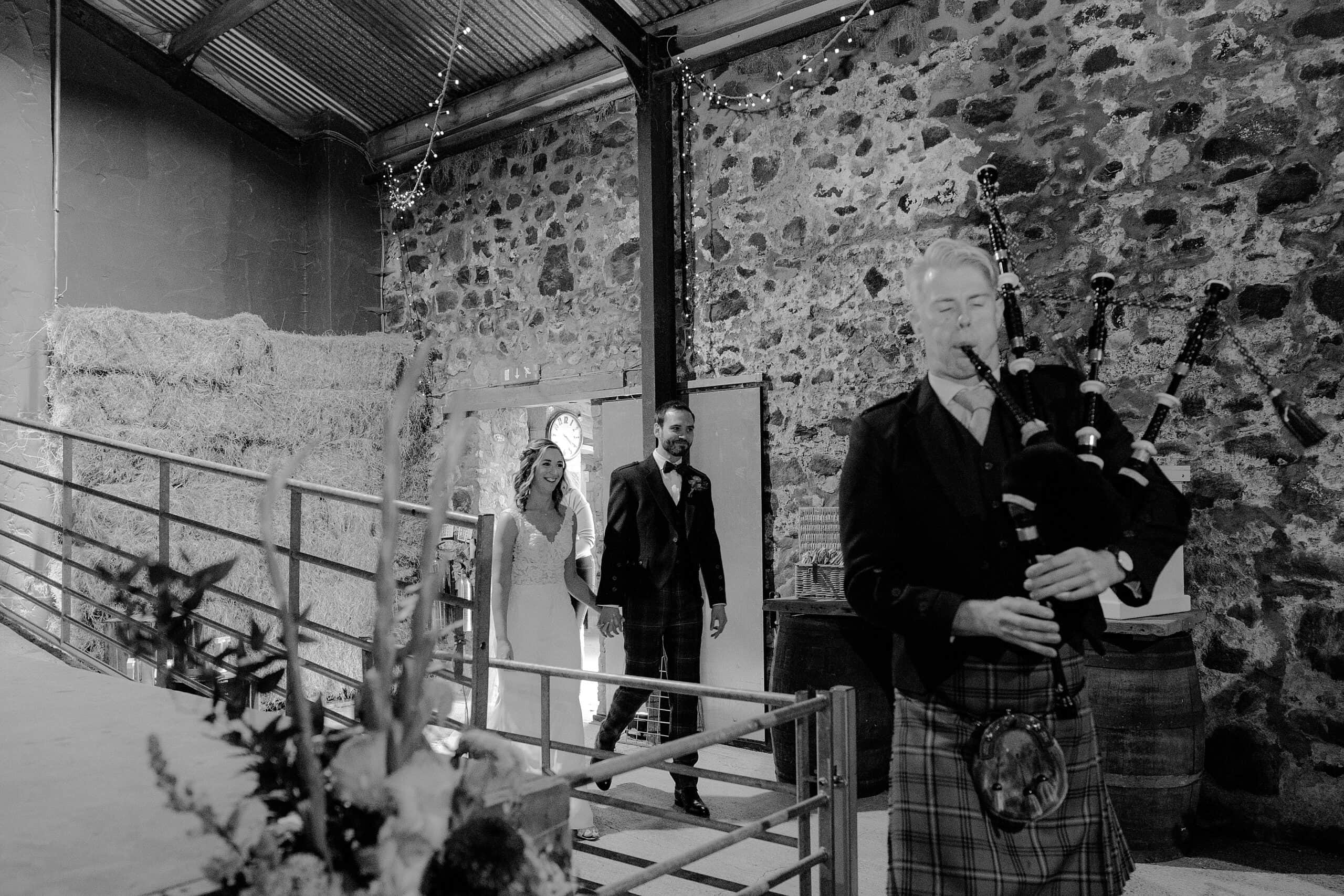 interior inside view of the hay barn at harelaw farm wedding barn venue fenwick scotland showing the bride and groom following piper into evening reception