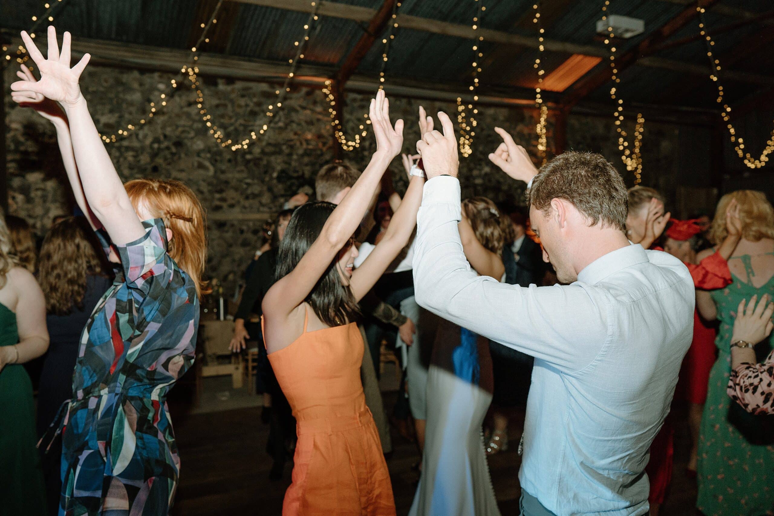 the wedding party dancing beneath festoon lights in the wedding barn at harelaw farm wedding venue fenwick scotland