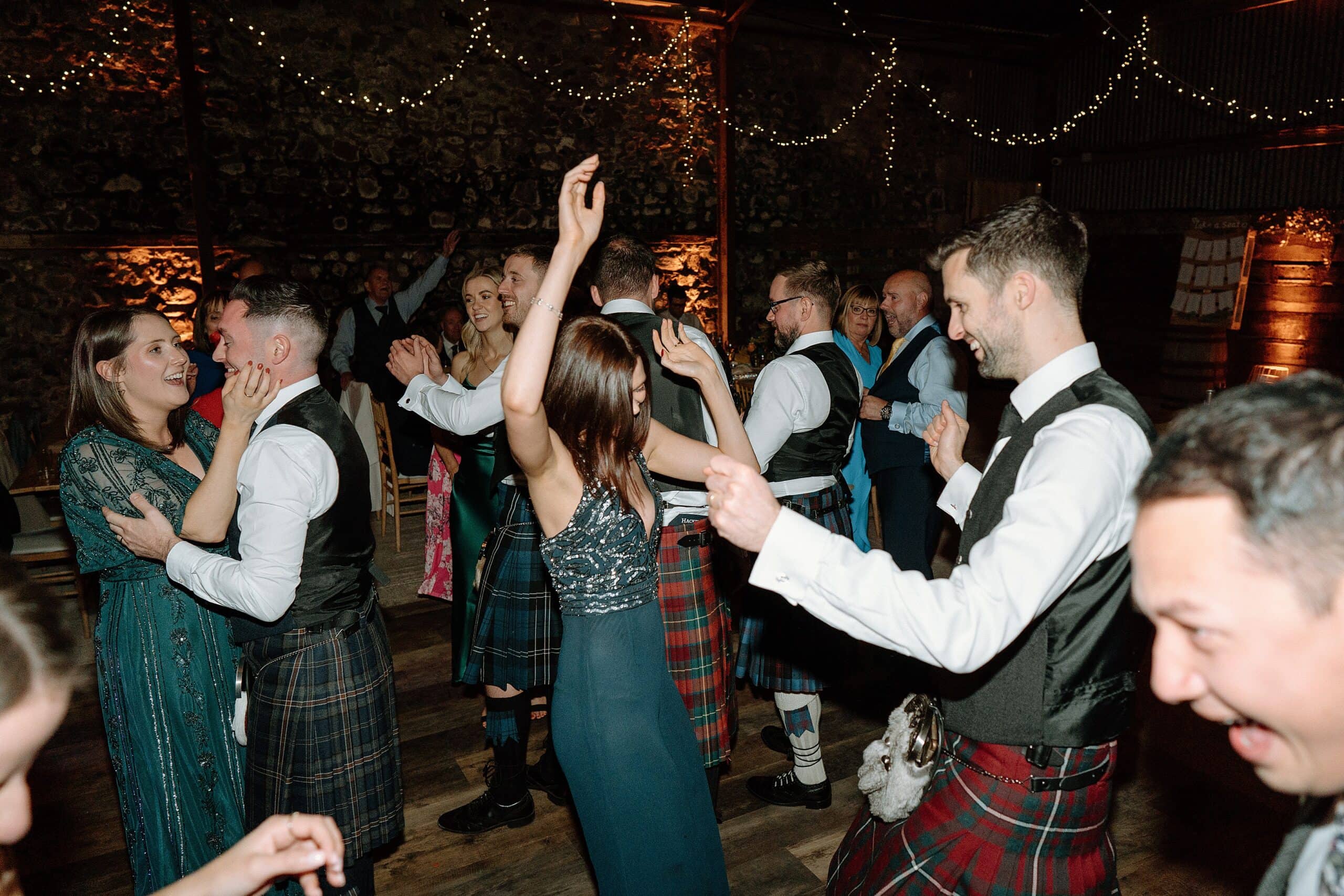 the wedding party dancing beneath festoon lights in the wedding barn at harelaw farm wedding venue fenwick scotland