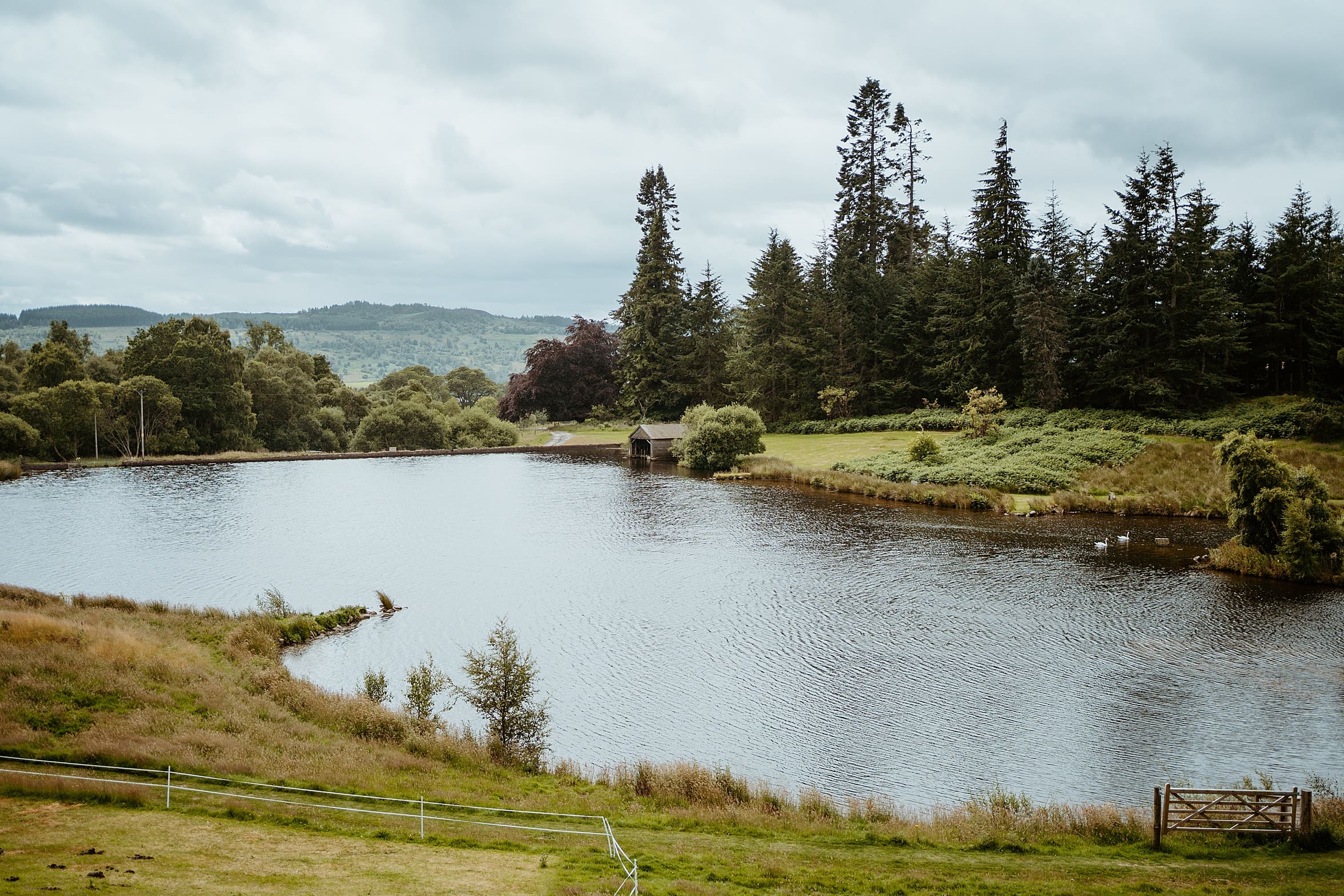 view of big pond on estate grounds with green trees and grass banks surrounding it cardney steading wedding perthshire