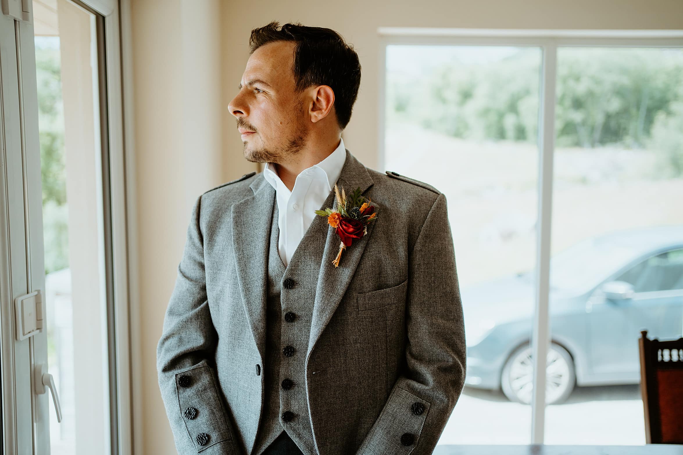 groom wearing grey tweed kilt outfit staring out of window cardney steading wedding photography