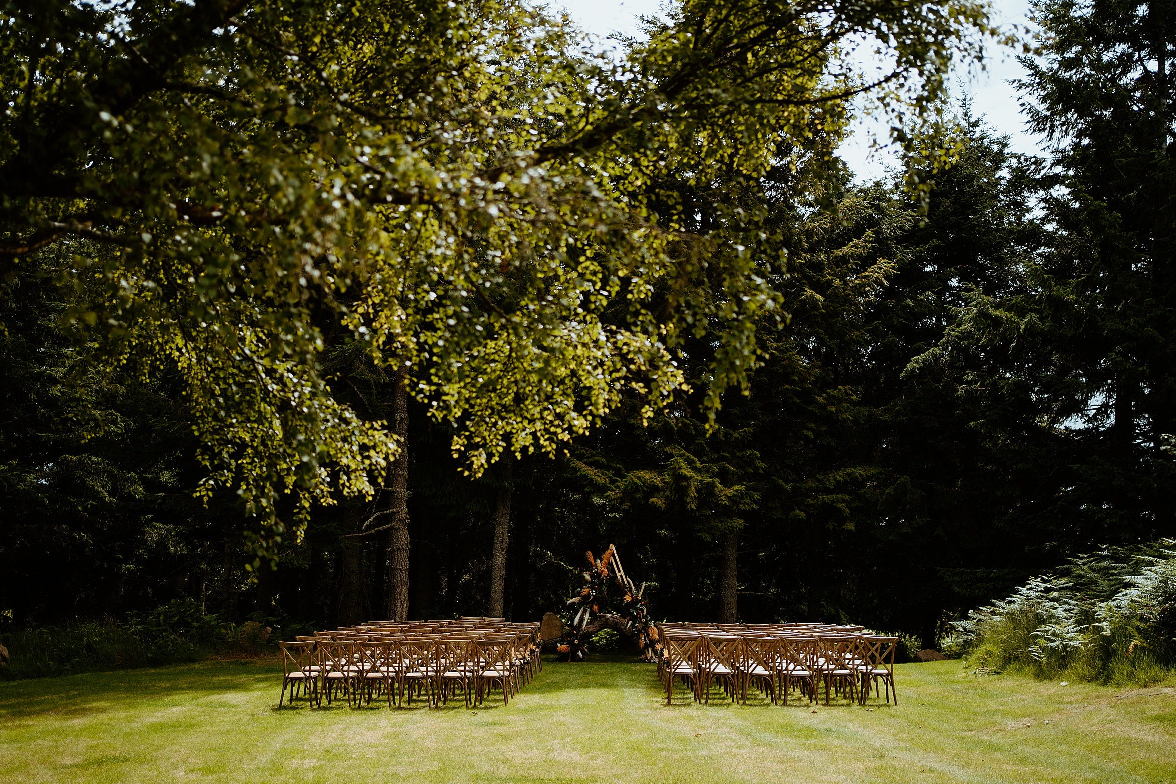 view of outdoor ceremony location before guests arrive rows of wooden seats on grass lawn in front of woodland cardney steading exclusive use wedding venue