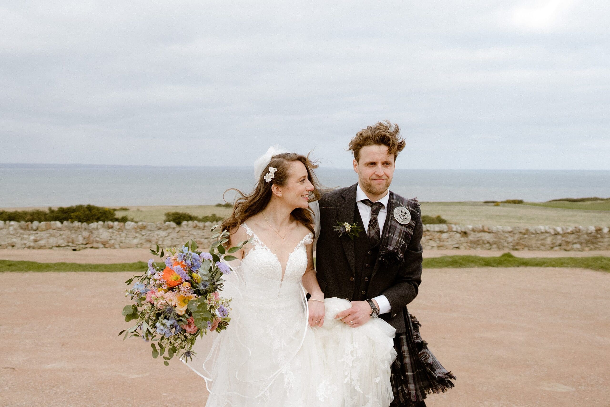 the bride and groom outside in scotland with the sea in the background photographed by st andrews wedding photographer