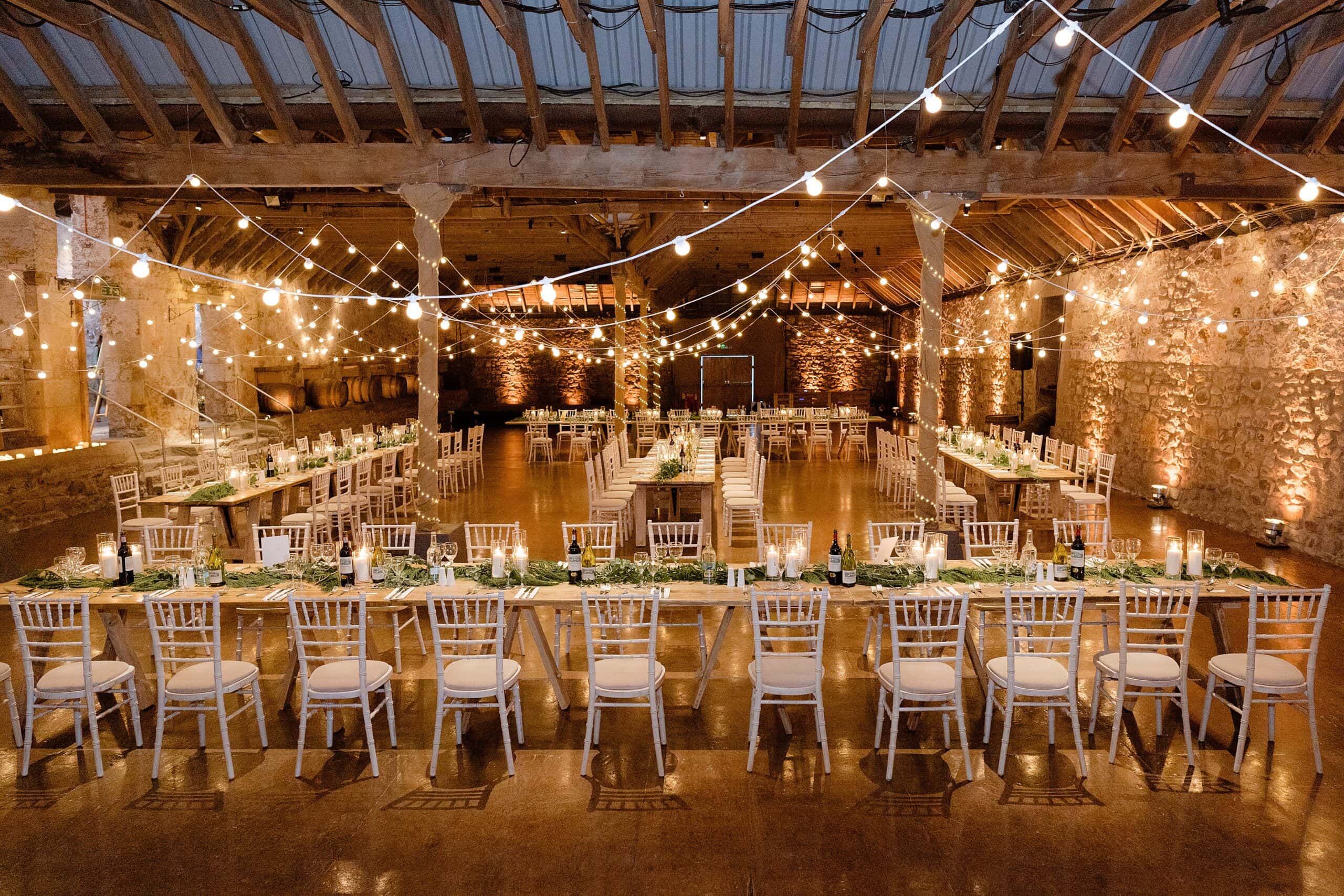 interior inside view of a scottish farm wedding venue with tables and chairs set for dinner with festoon lights and wooden beams above photographed by st andrews wedding photographer