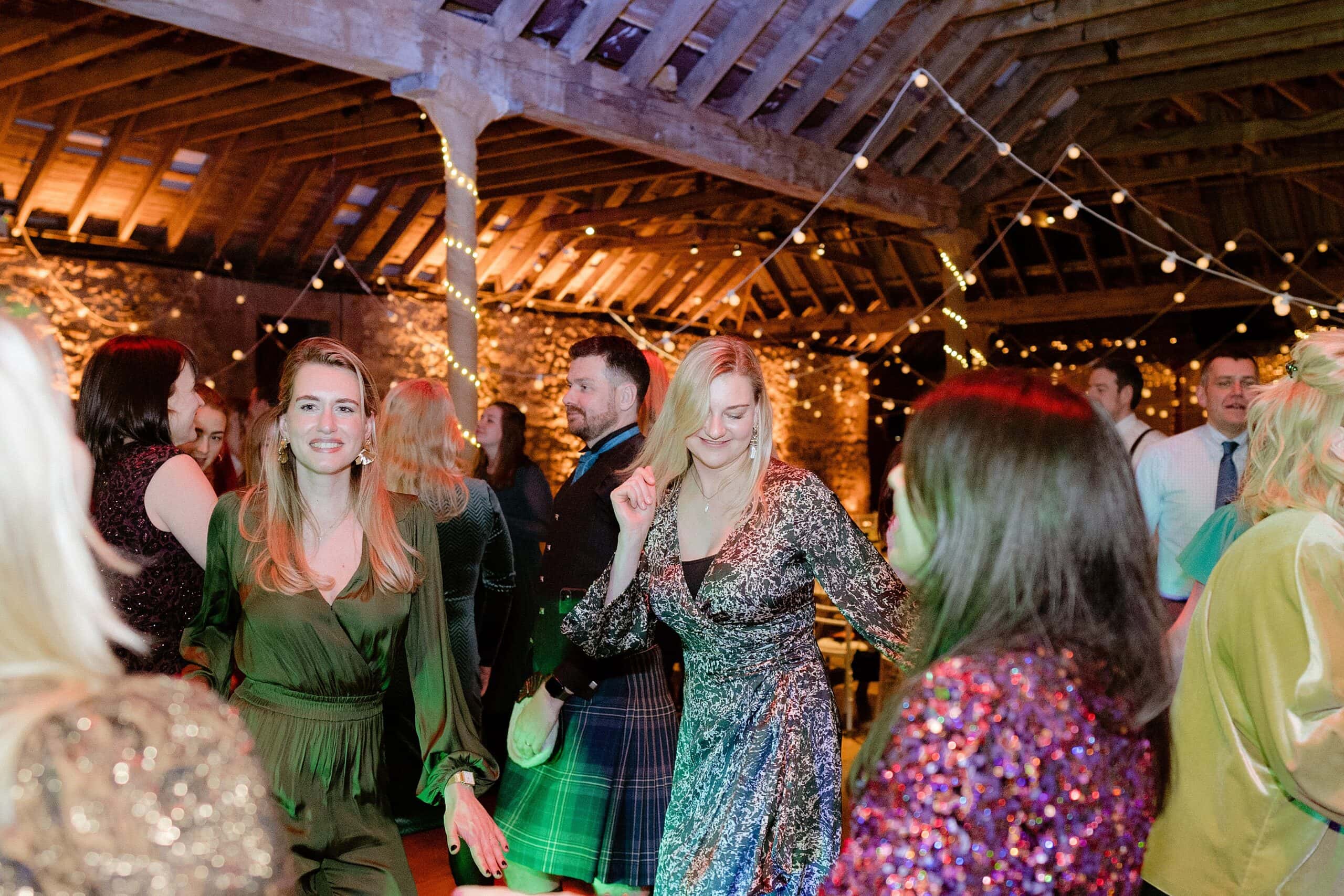 st andrews wedding photographer captures guests dancing underneath wooden beams and festoon lights at a unique farm wedding venue in scotland