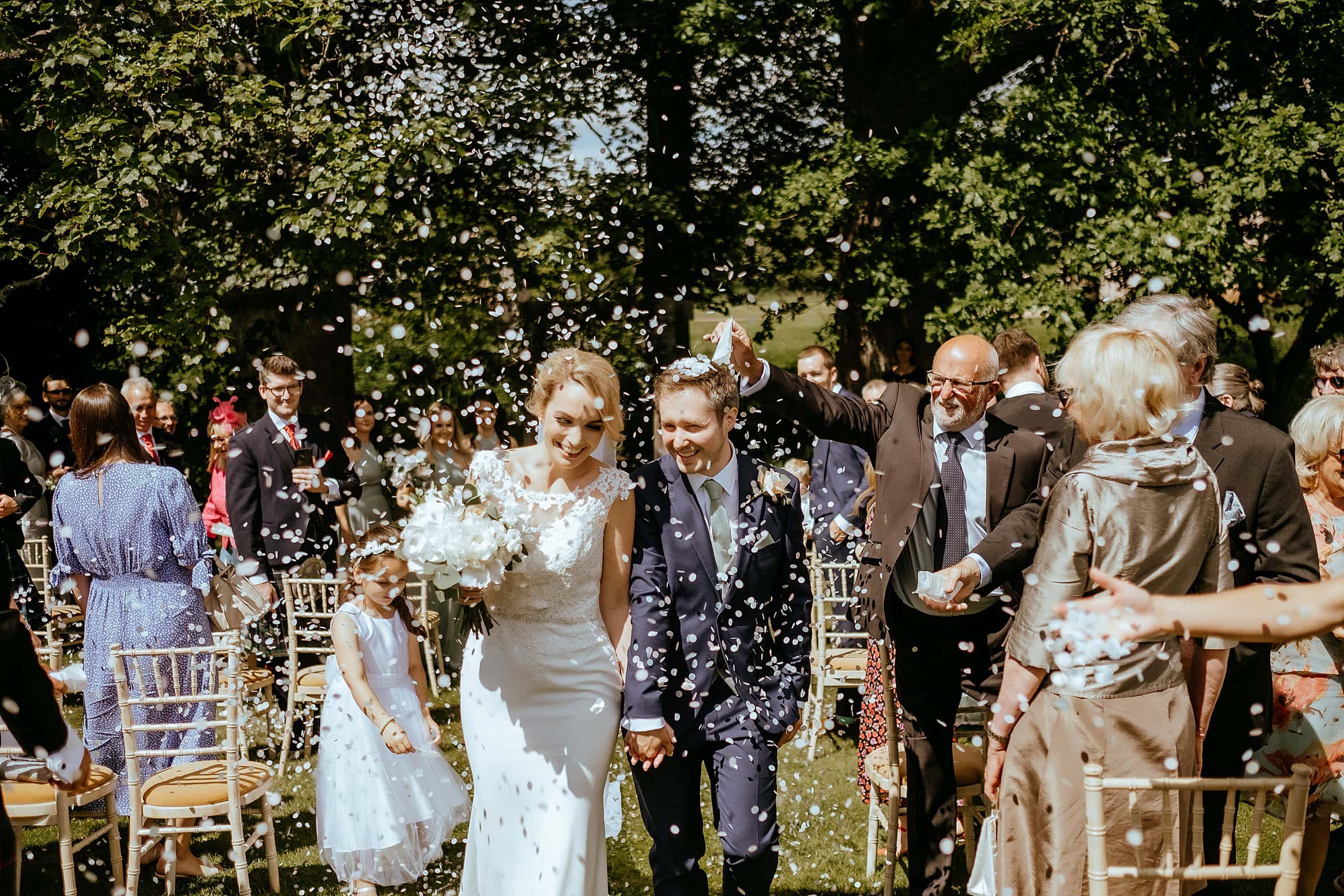 just married bride and groom walking back down the aisle as guests shower them in confetti on sunny day exclusive use colstoun house wedding unique wedding venue scotland