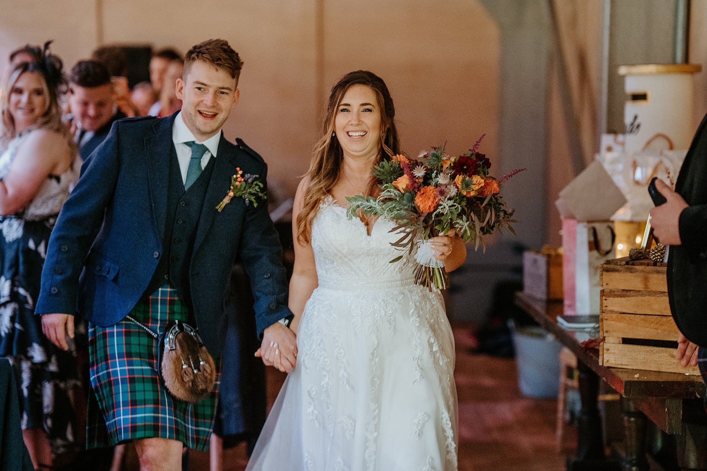 bride in white dress and groom wearing kilt outfit walking hand in hand as they enter the reception in marquee duntarvie castle wedding