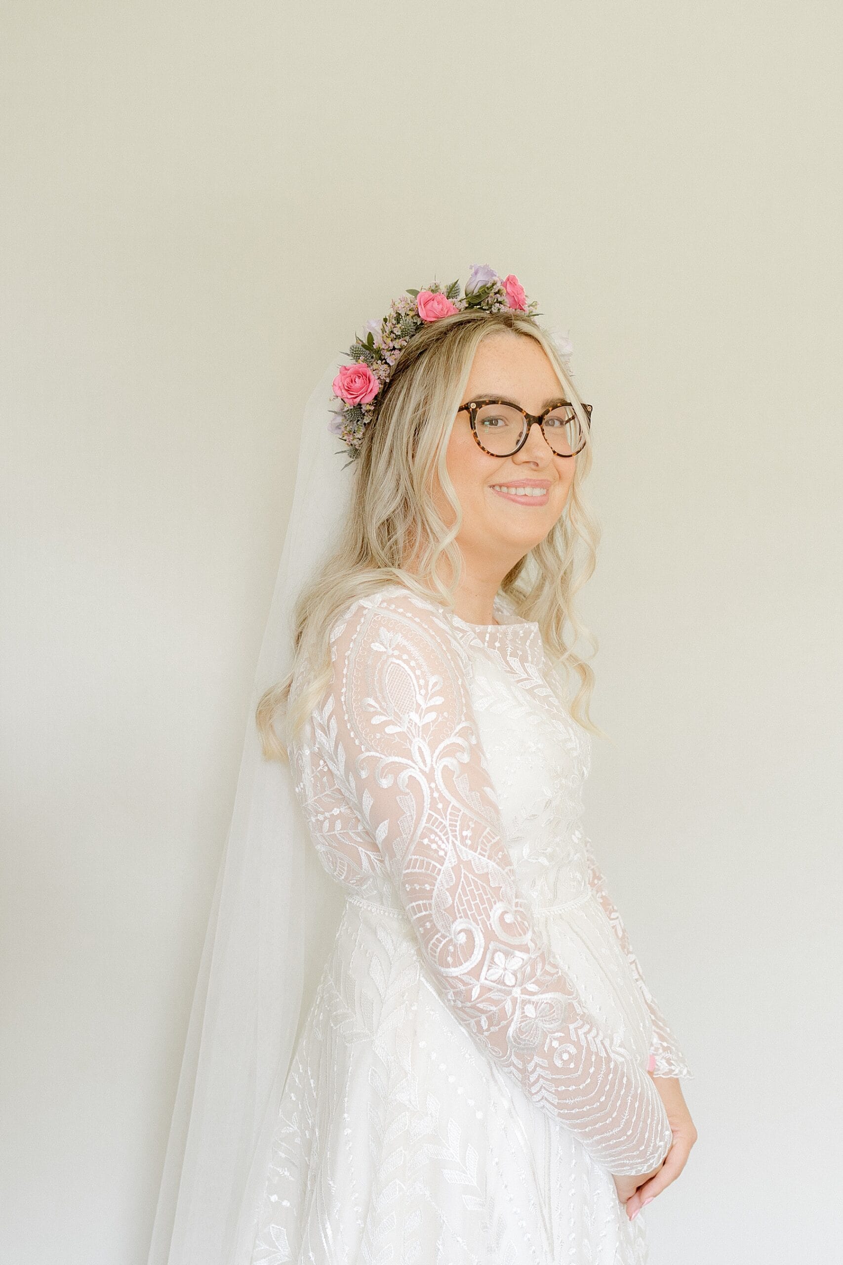 bridal portrait of bride wearing a white lace dress with sleeves and a pink flower crown before her ceremony at the den at culross wedding