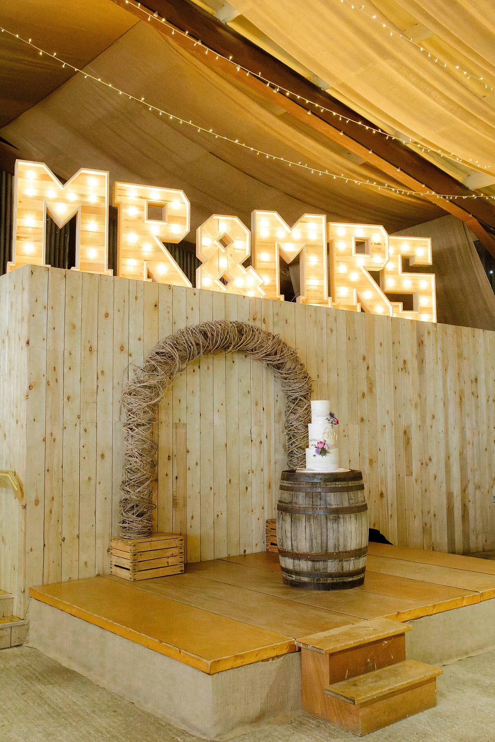 huge mr and mrs wedding lights inside barn with willow arch and whisky barrel for the den at culross wedding