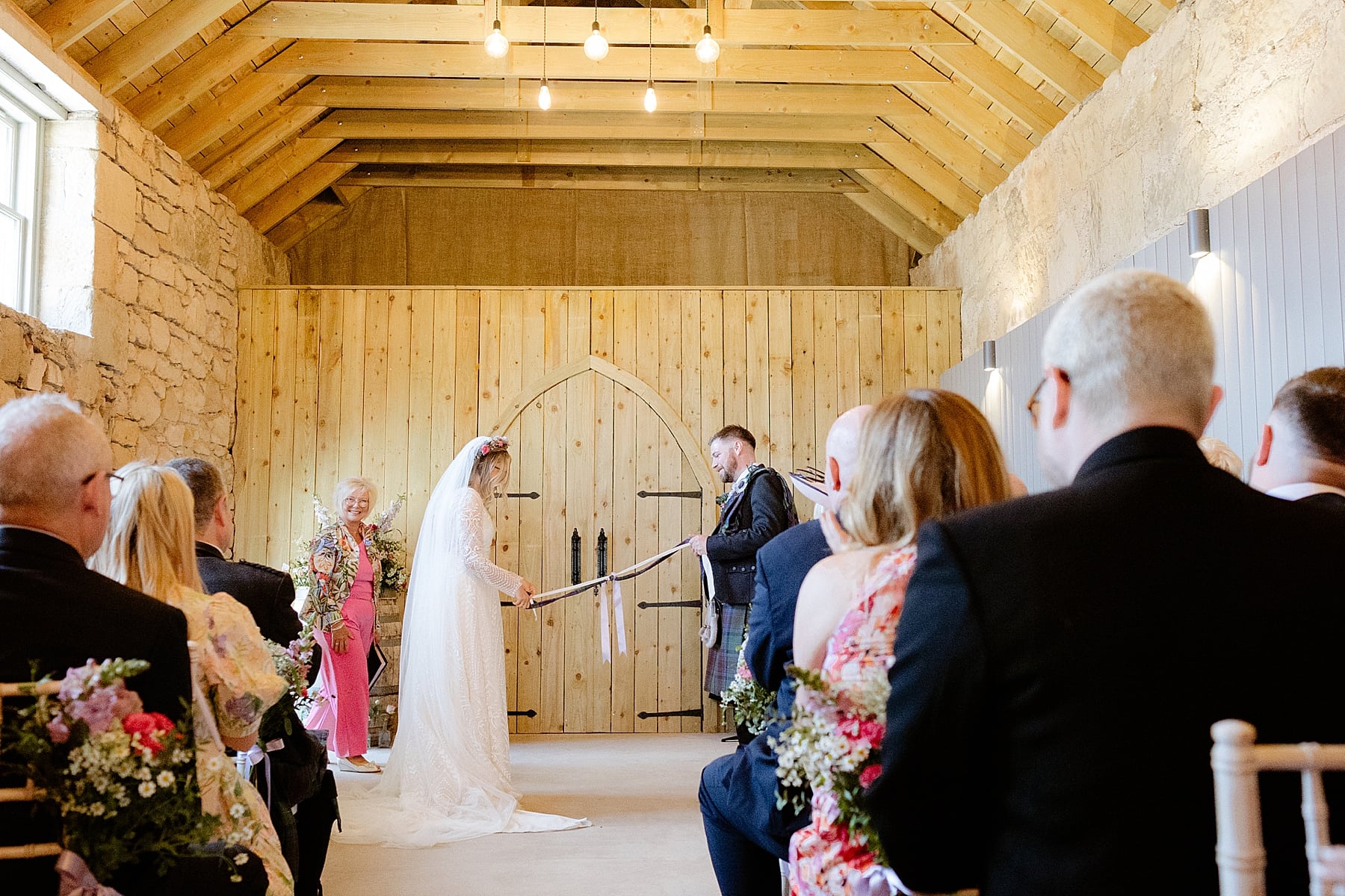 bride and groom during hand fasting ceremony at their the den at culross wedding inside wooden barn