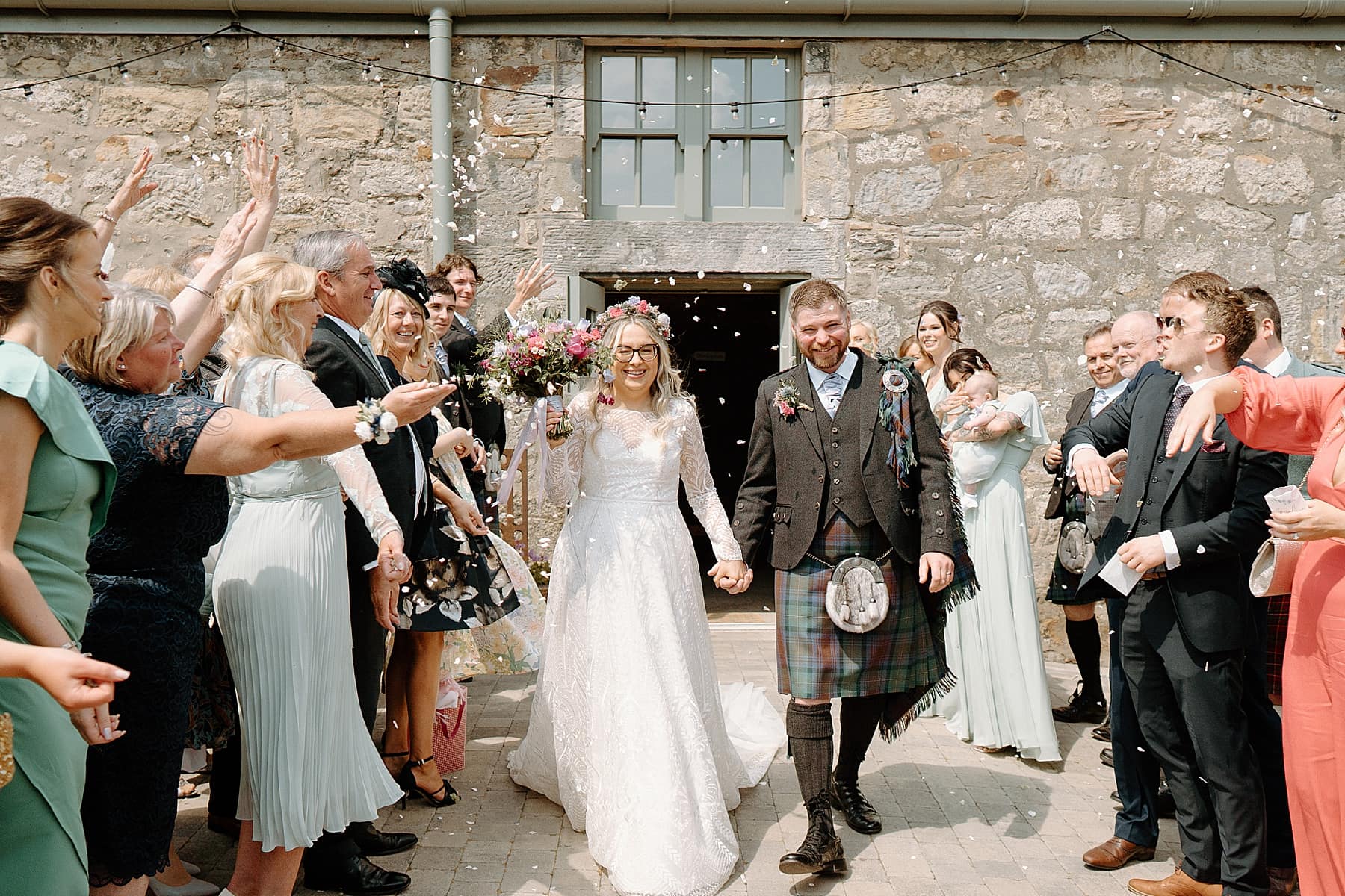 bride and groom walking under confetti throw on sunny day at their small barn wedding scotland
